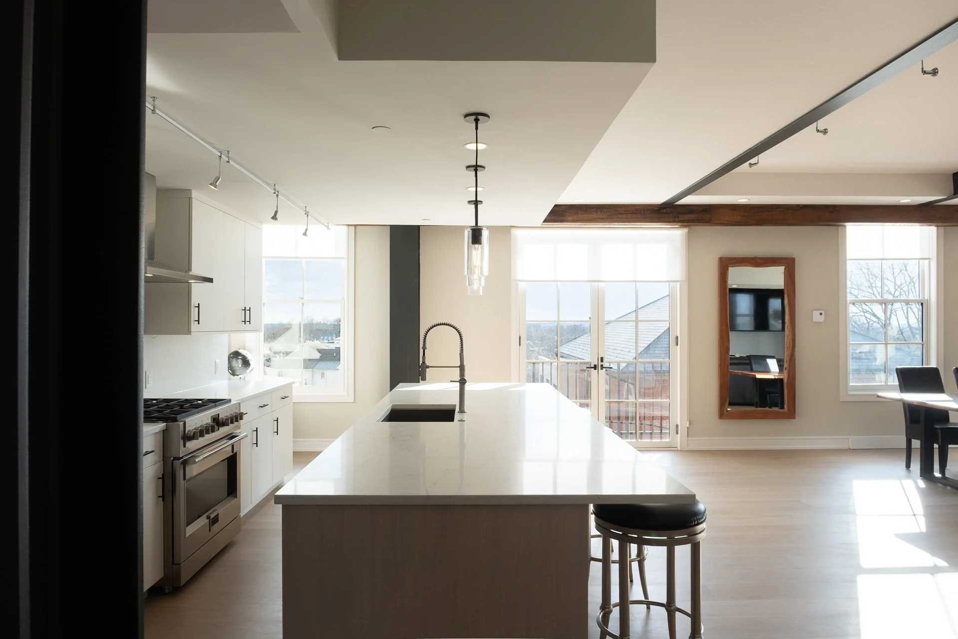 Modern kitchen with white cabinets, a large white countertop island with a black sink, a pendant light hanging above, and a view of windows and a balcony door letting in natural light.