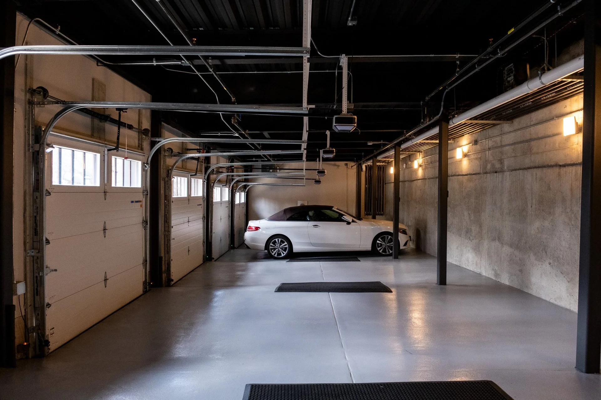 Empty garage with a white convertible car parked inside, multiple garage doors, and overhead lighting.
