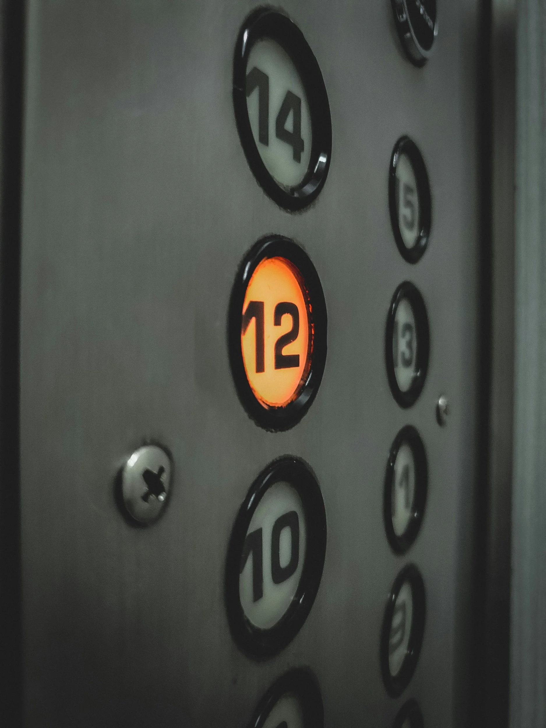 Elevator control panel with illuminated button for the 12th floor and other floor buttons nearby.