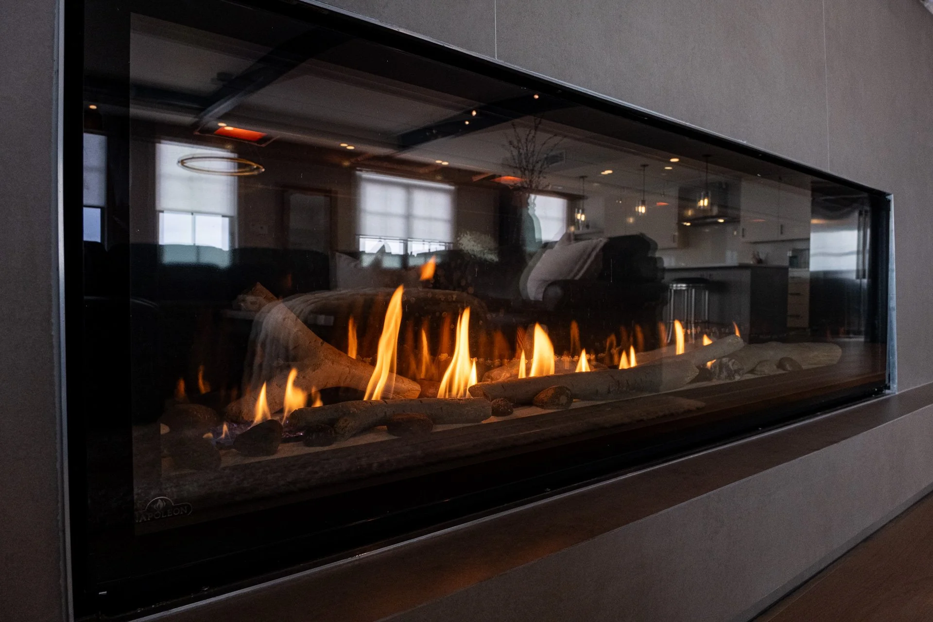 Modern indoor fireplace with visible flames and decorative logs, situated in a contemporary living space with large windows and soft lighting.