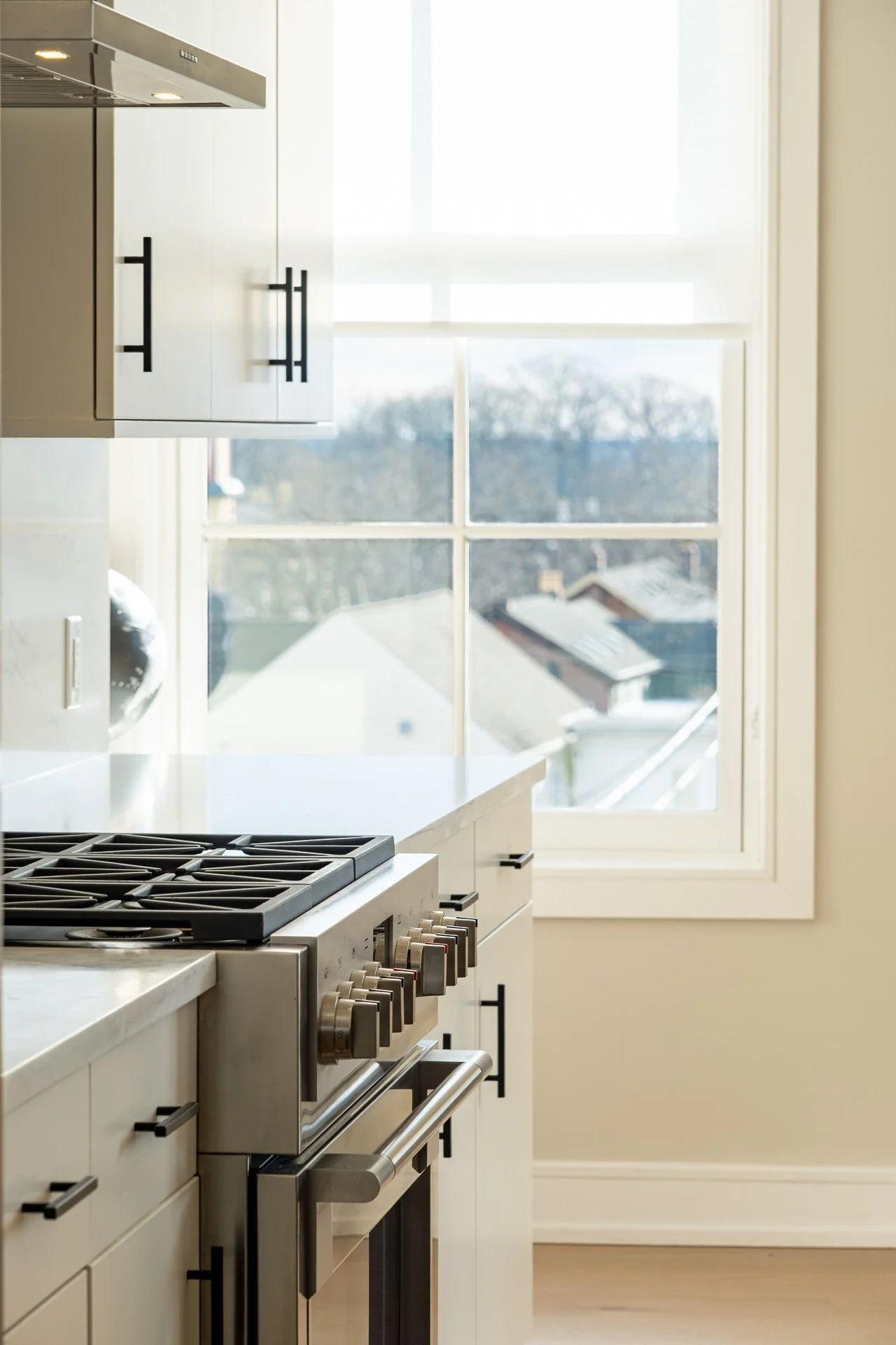 Modern kitchen with beige cabinets, a large window, and a stainless steel gas oven.