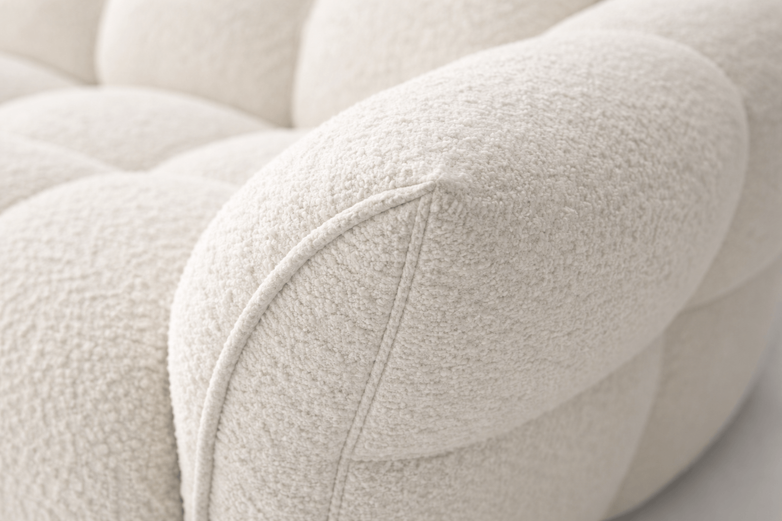 Close-up of a cream-colored, textured fabric armrest of a sofa with piping detail