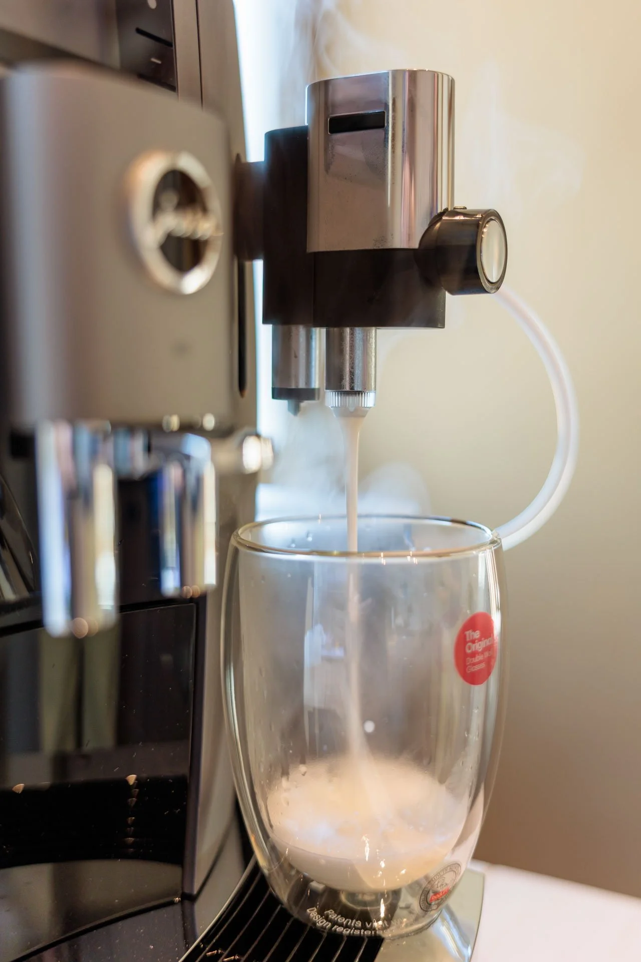 Een koffiezetapparaat dat melk uit een roestvrijstalen kunnen spuit in een doorzichtige glazen mok. Melk wordt gespoten en schuimt op.