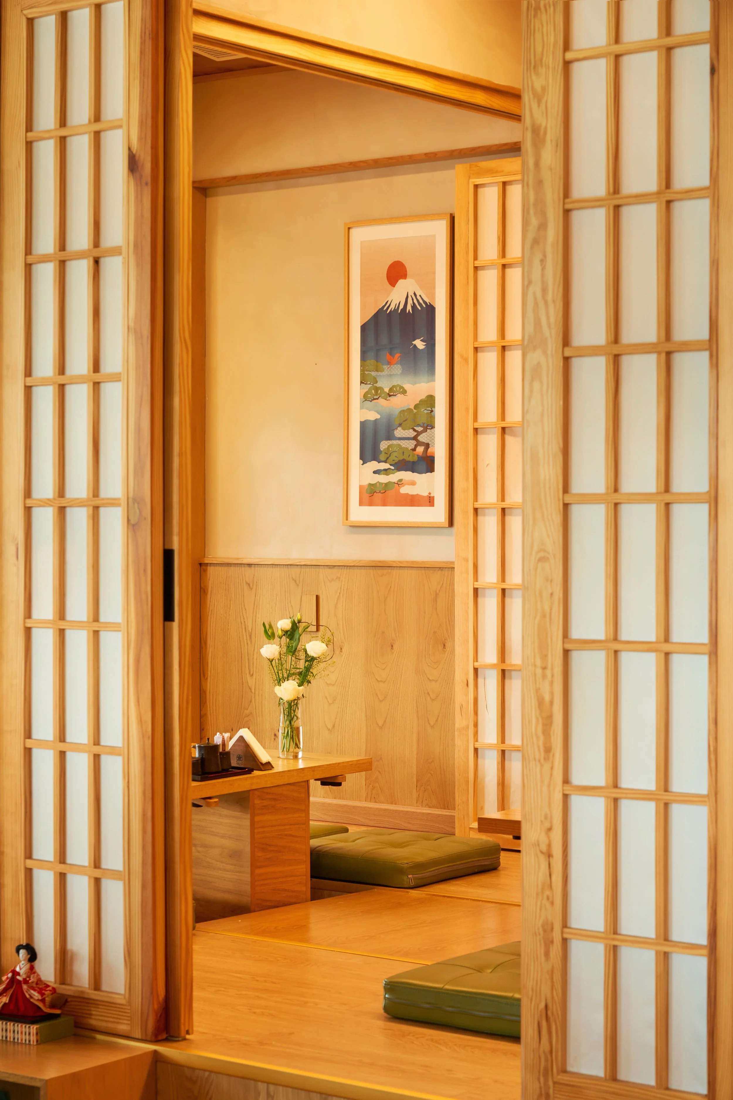 Interior of a traditional Japanese room with wooden elements, sliding shoji doors, a low wooden table with flower arrangement, and tatami mats.