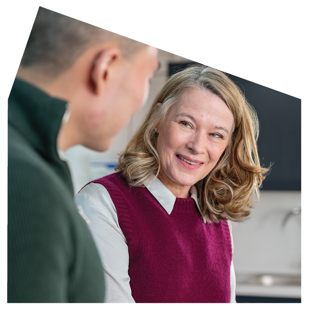 A woman with blonde, wavy hair smiling and looking at a man whose face is not visible.