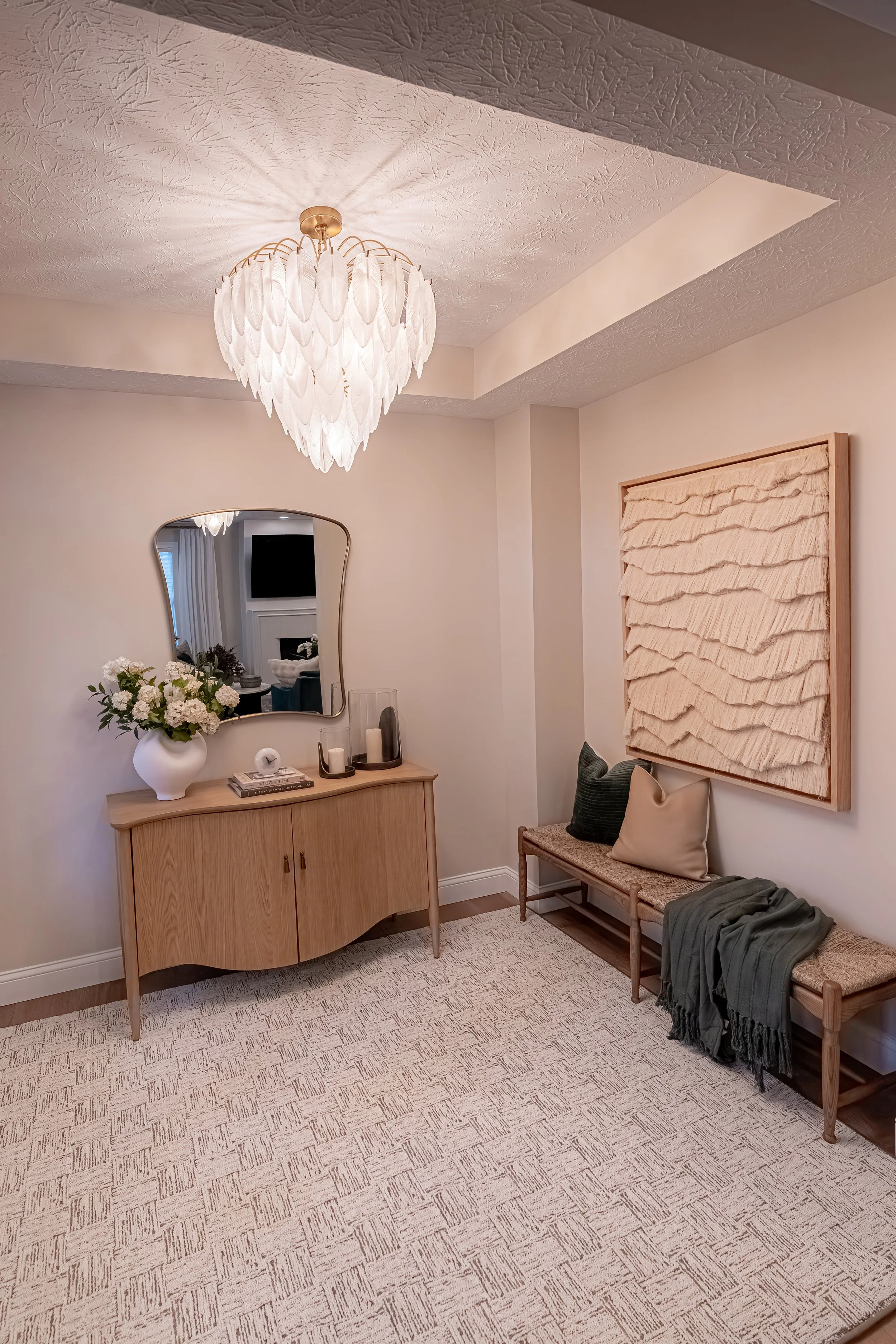 Designed entryway with a white oak console table, curved mirror, feather chandelier, textured wall art, and a wood bench in an Oakwood, Ohio home
