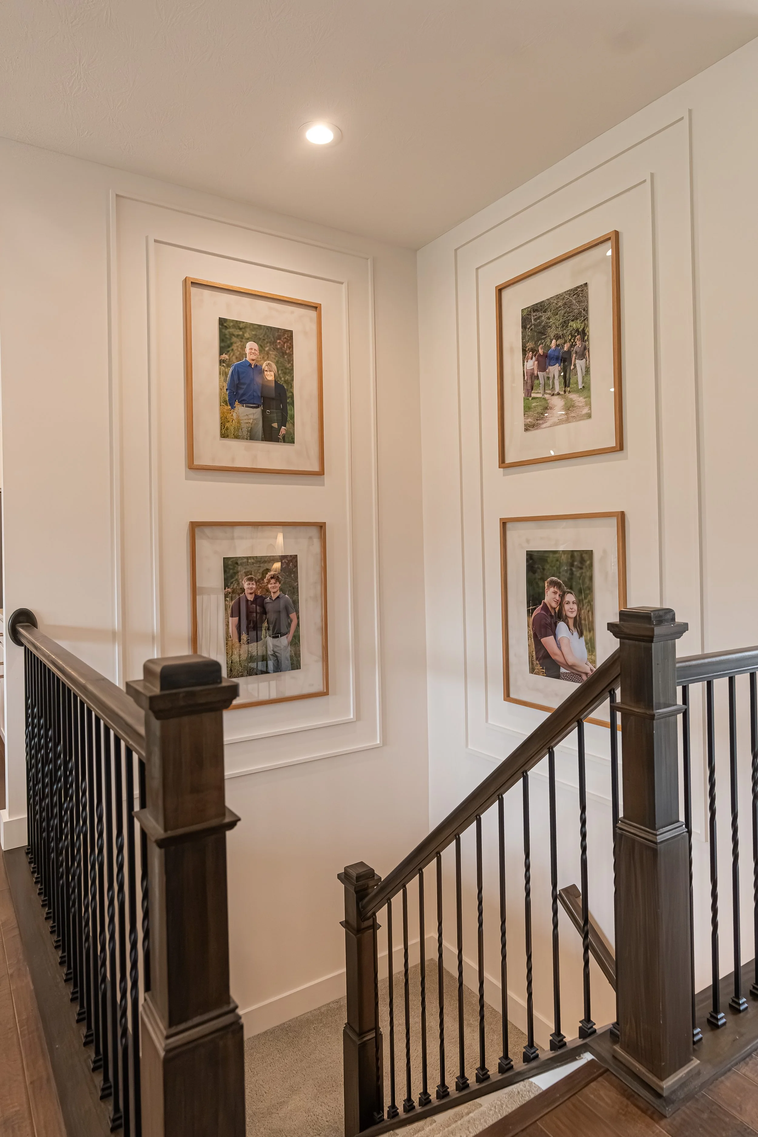 Staircase with a wood railing, black metal balusters, and a framed family gallery wall in a Centerville home renovation.