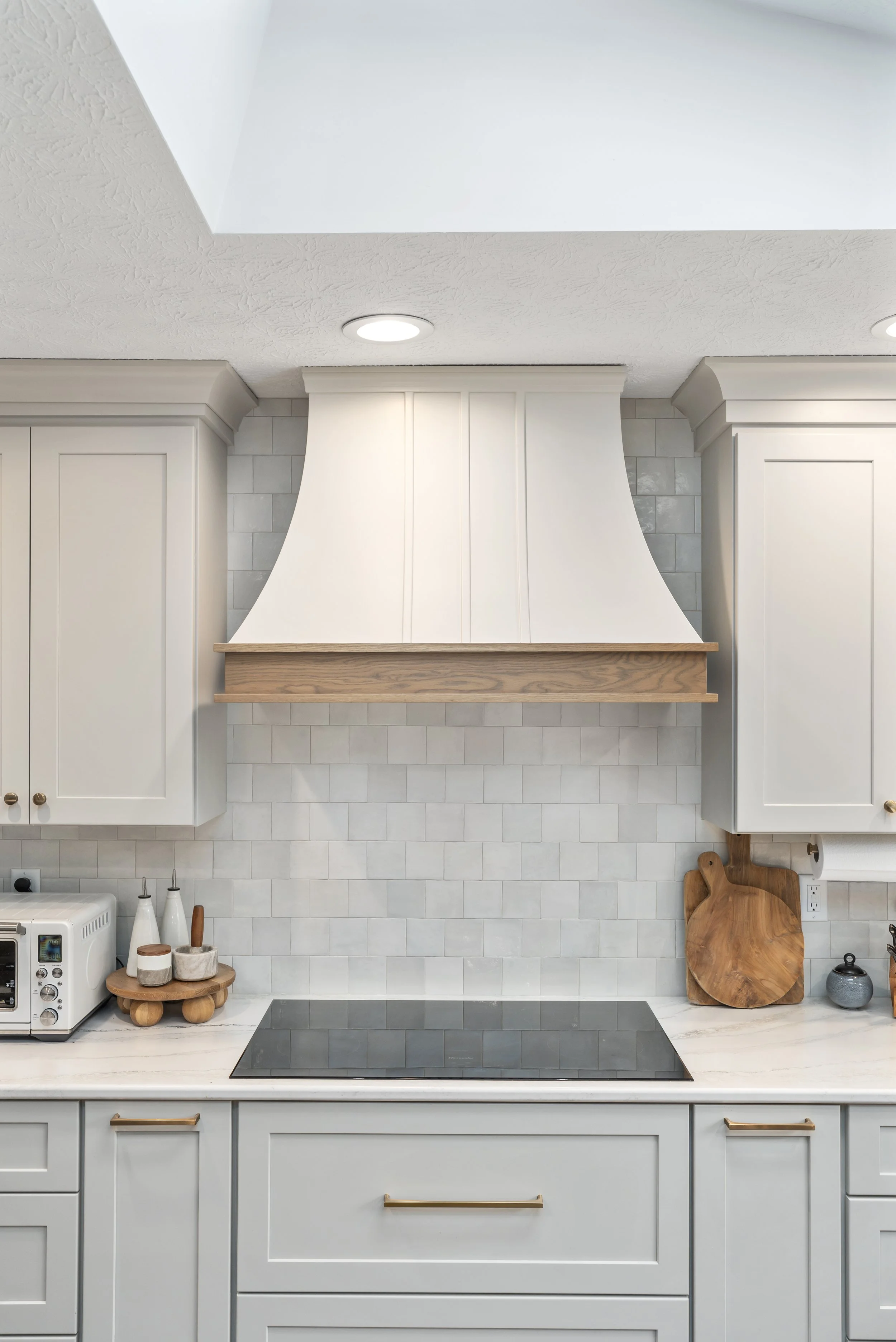 Close-up of a custom curved white range hood with a stained wood accent band and white subway tile backsplash