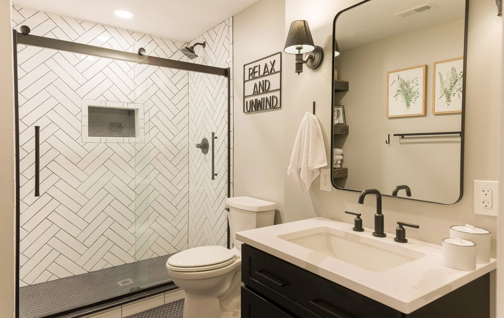Black basement vanity with backlit mirror and sconces beside a herringbone-tiled shower near Dayton, Ohio