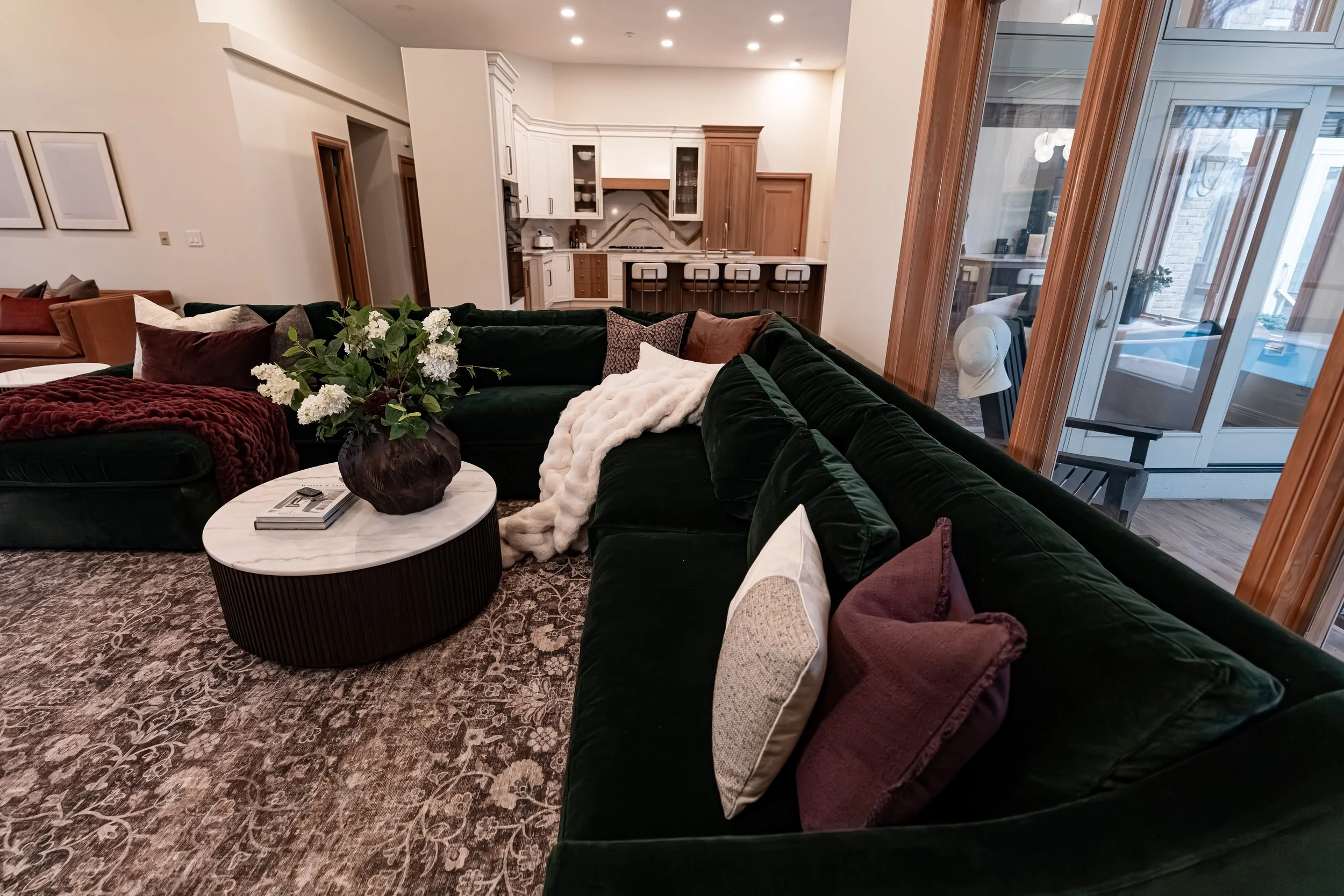 Green velvet sectional and fluted marble-top coffee table with the kitchen beyond in a Bellbrook, Ohio open-concept remodel