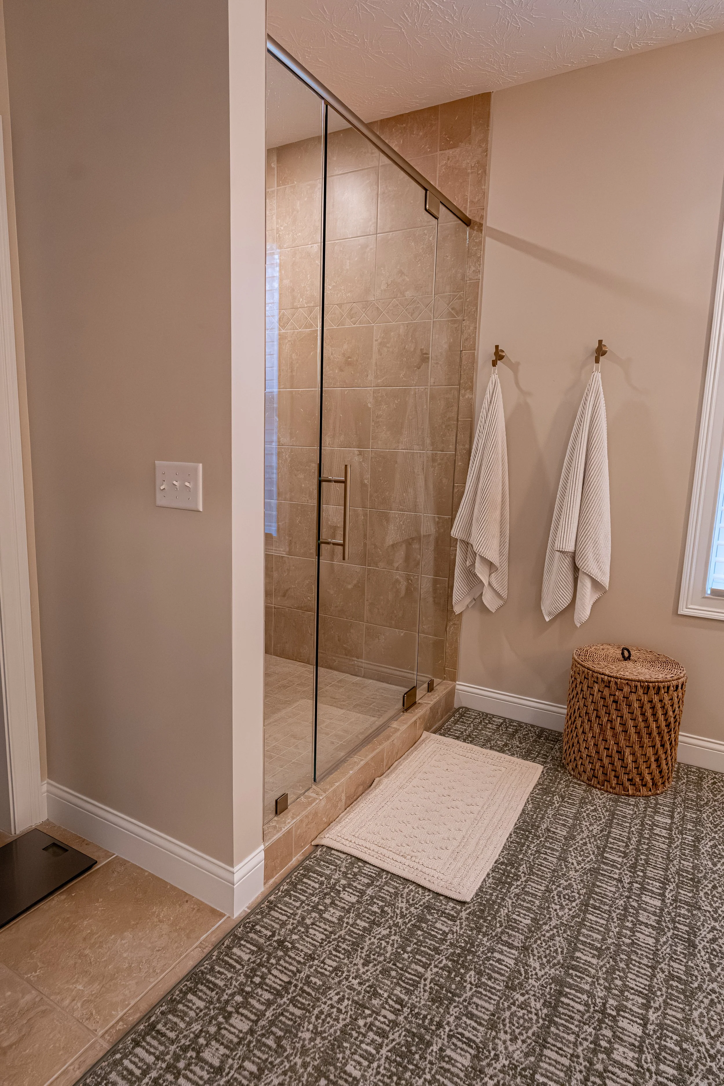 Enlarged glass-enclosed master shower with stone-look tile, updated shower system, and warm neutral tones in an Oakwood, Ohio renovation
