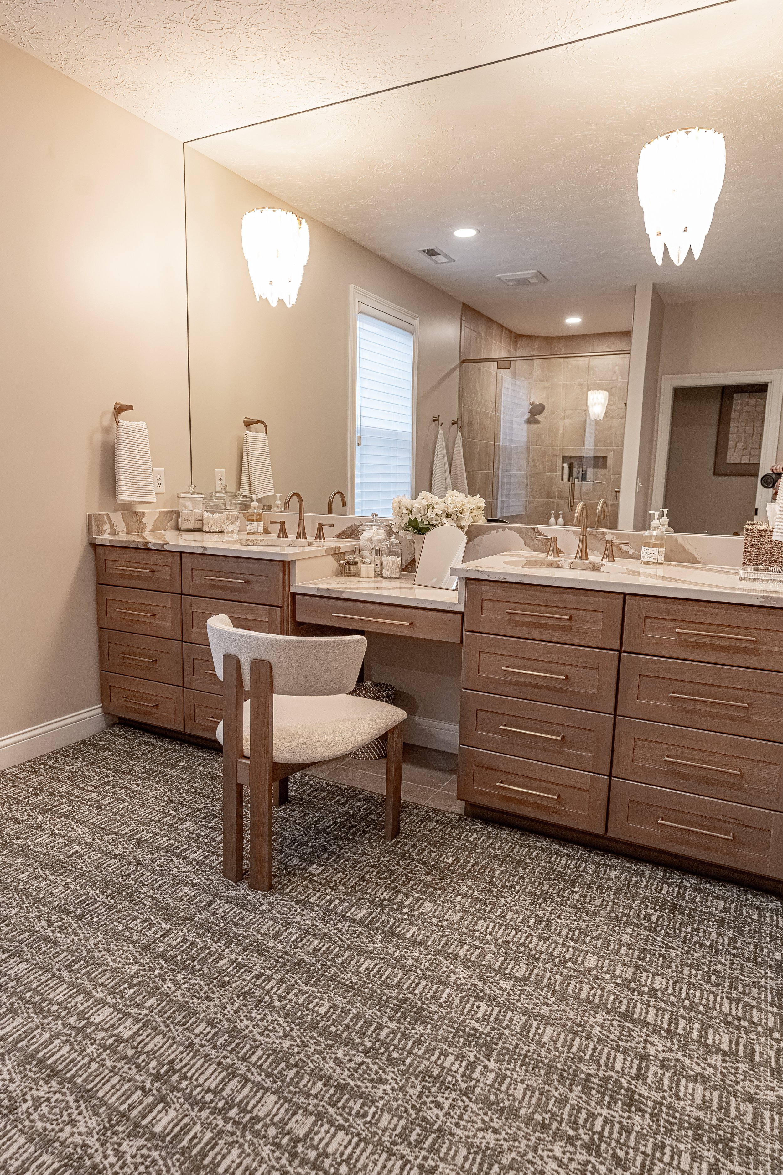 Master bathroom with a custom full-wall mirror, white oak double vanity, integrated makeup desk, Britannica Gold quartz countertops, and patterned carpet