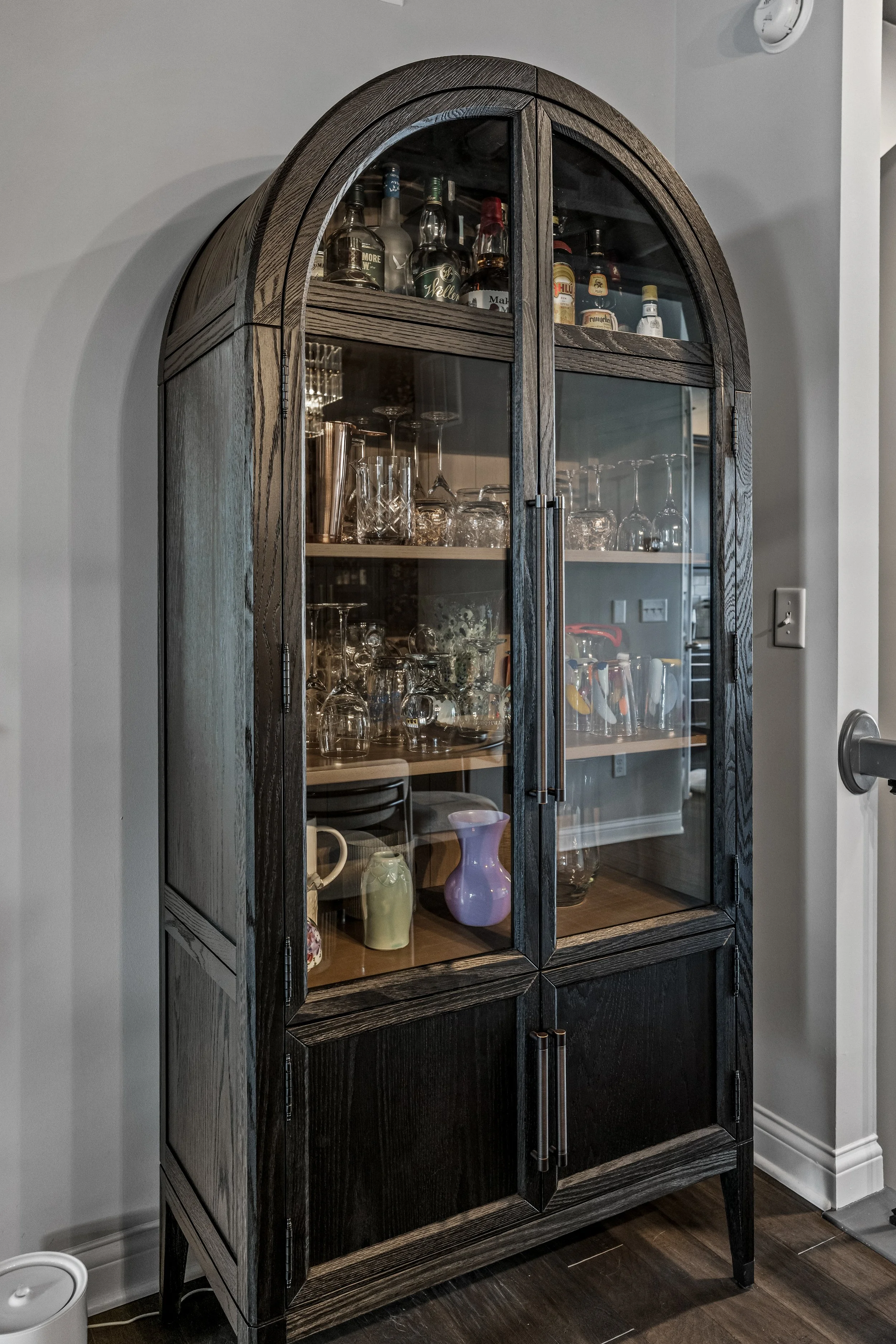 Arched glass-front bar cabinet with barware and glassware storage in a Springboro, Ohio home by White Oak Interiors