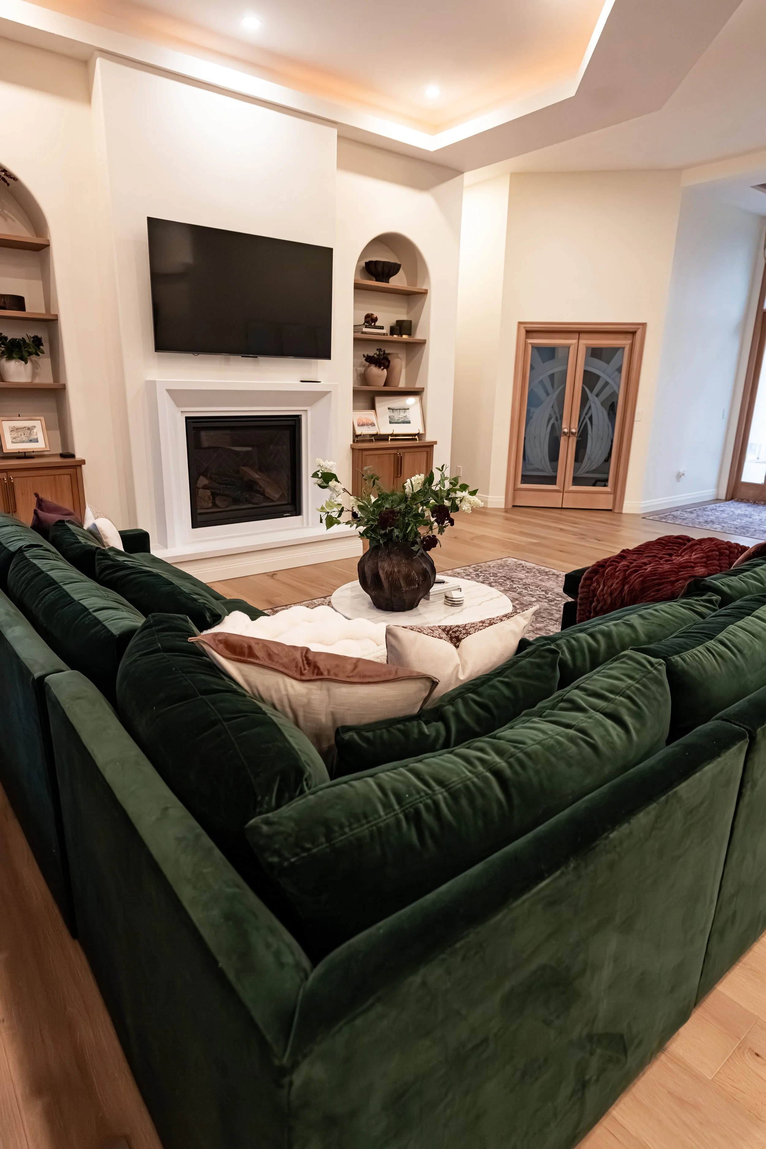 Bellbrook, Ohio living room with fireplace, arched built-in shelving, and green velvet sectional by White Oak Interiors