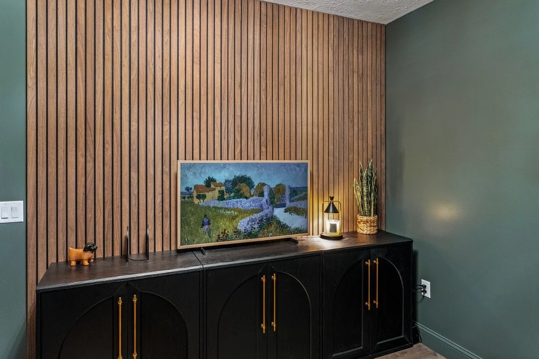Basement bar area with a wood-slat accent wall and a black arched cabinet with brass pulls in a Brookville, Ohio basement renovation.