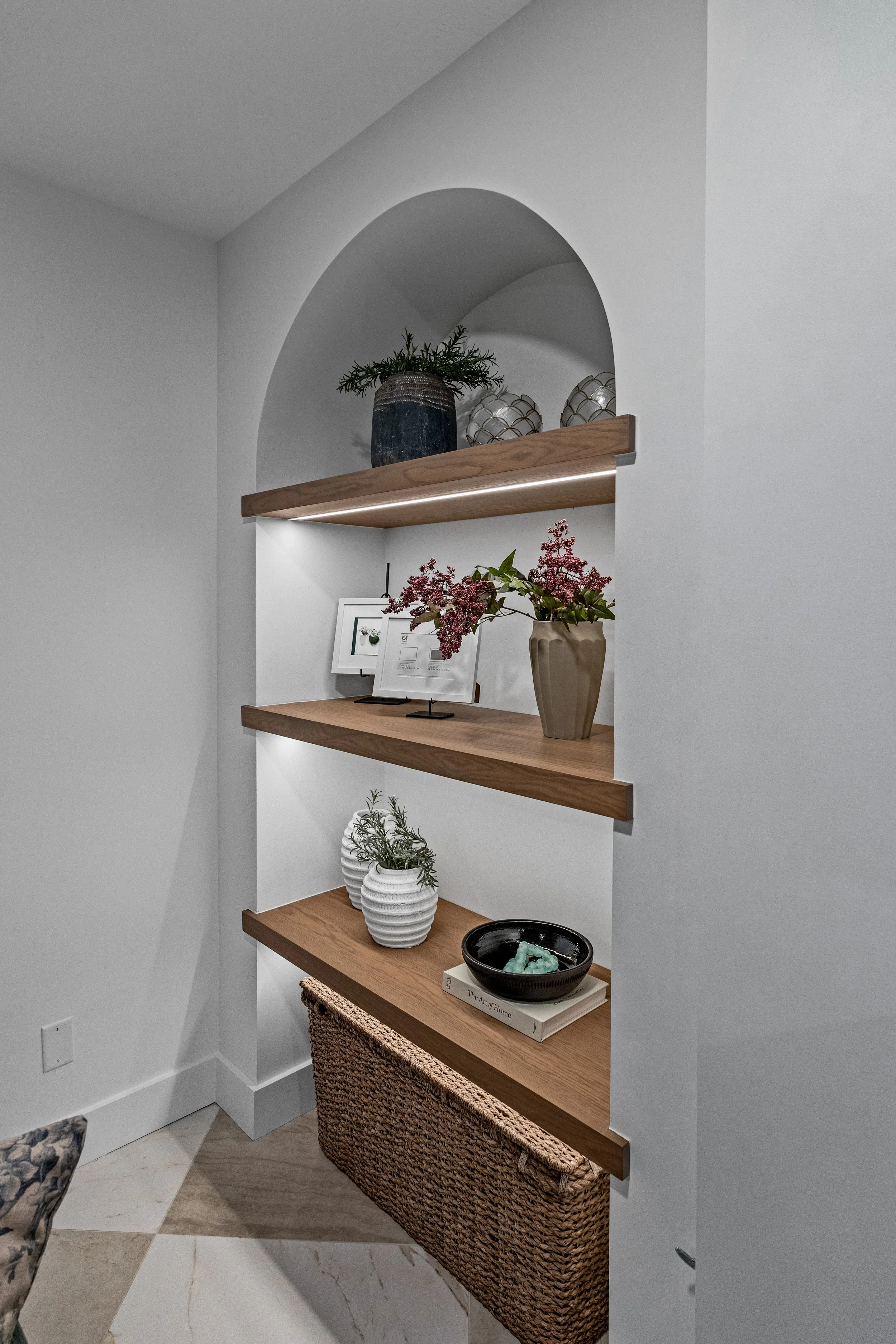 Styled custom arched niche with lit walnut floating shelves in a Centerville, Ohio finished basement by White Oak Interiors