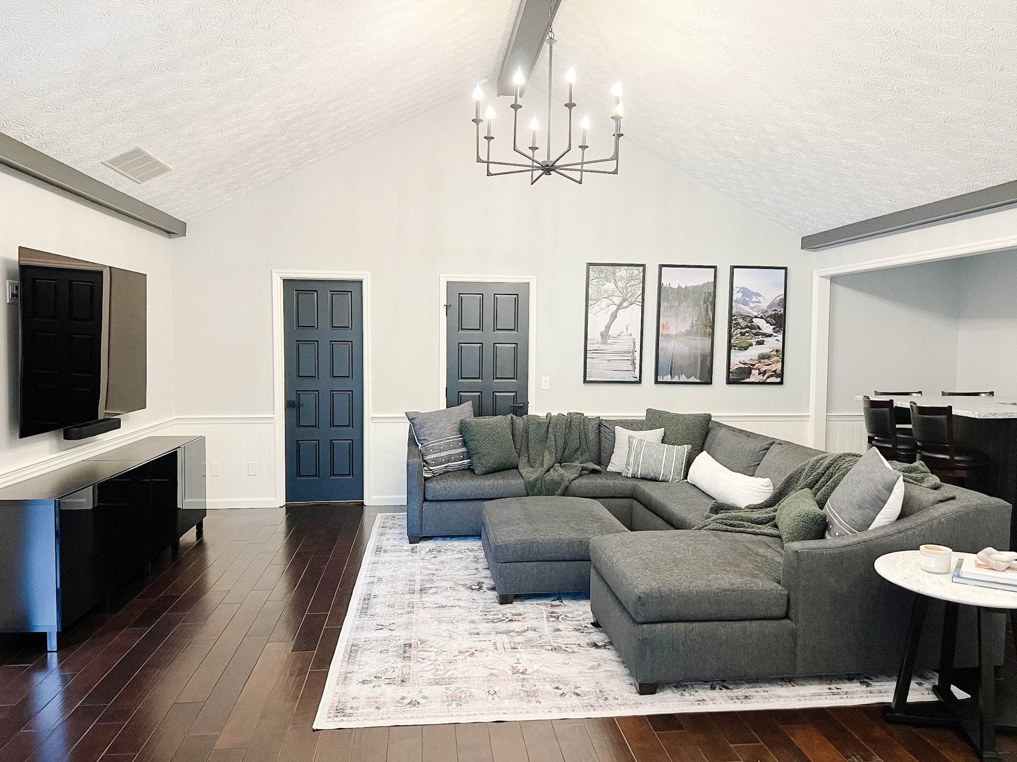 Living room with a gray sectional, framed gallery wall, dark double doors, a vaulted ceiling, and dark wood flooring in a Centerville, Ohio renovation
