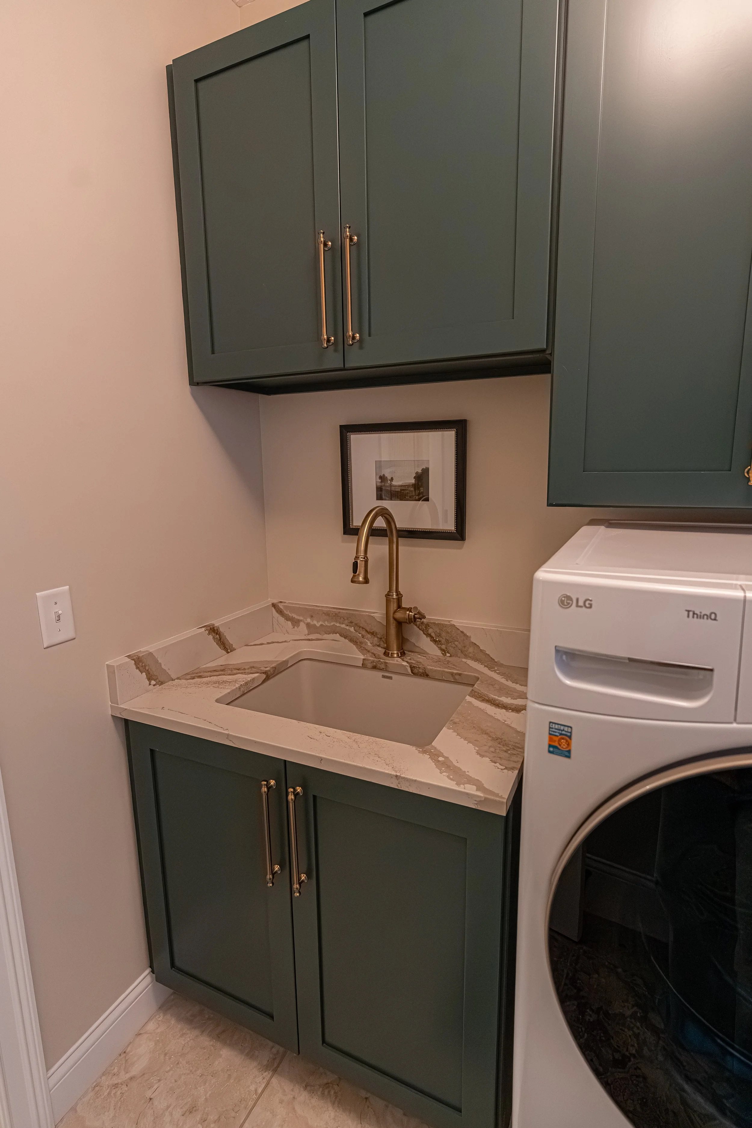 Laundry room detail with green shaker cabinetry, brass hardware, a quartz countertop, undermount sink, and brushed gold faucet in an Oakwood, Ohio home