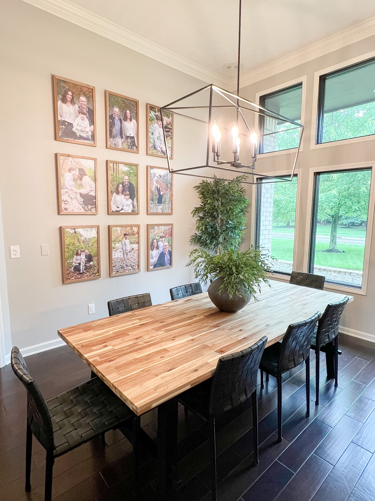 Dining room with a wood table, black upholstered chairs, a linear chandelier, a framed family gallery wall, and large windows in a Centerville, Ohio home