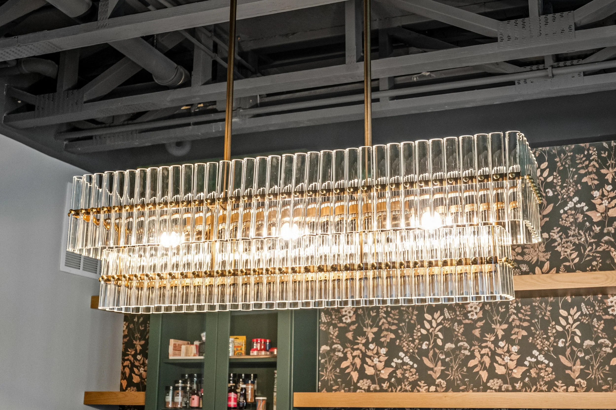 Crystal linear chandelier over wallpapered dining built-ins and bar in a Springboro, Ohio home by White Oak Interiors