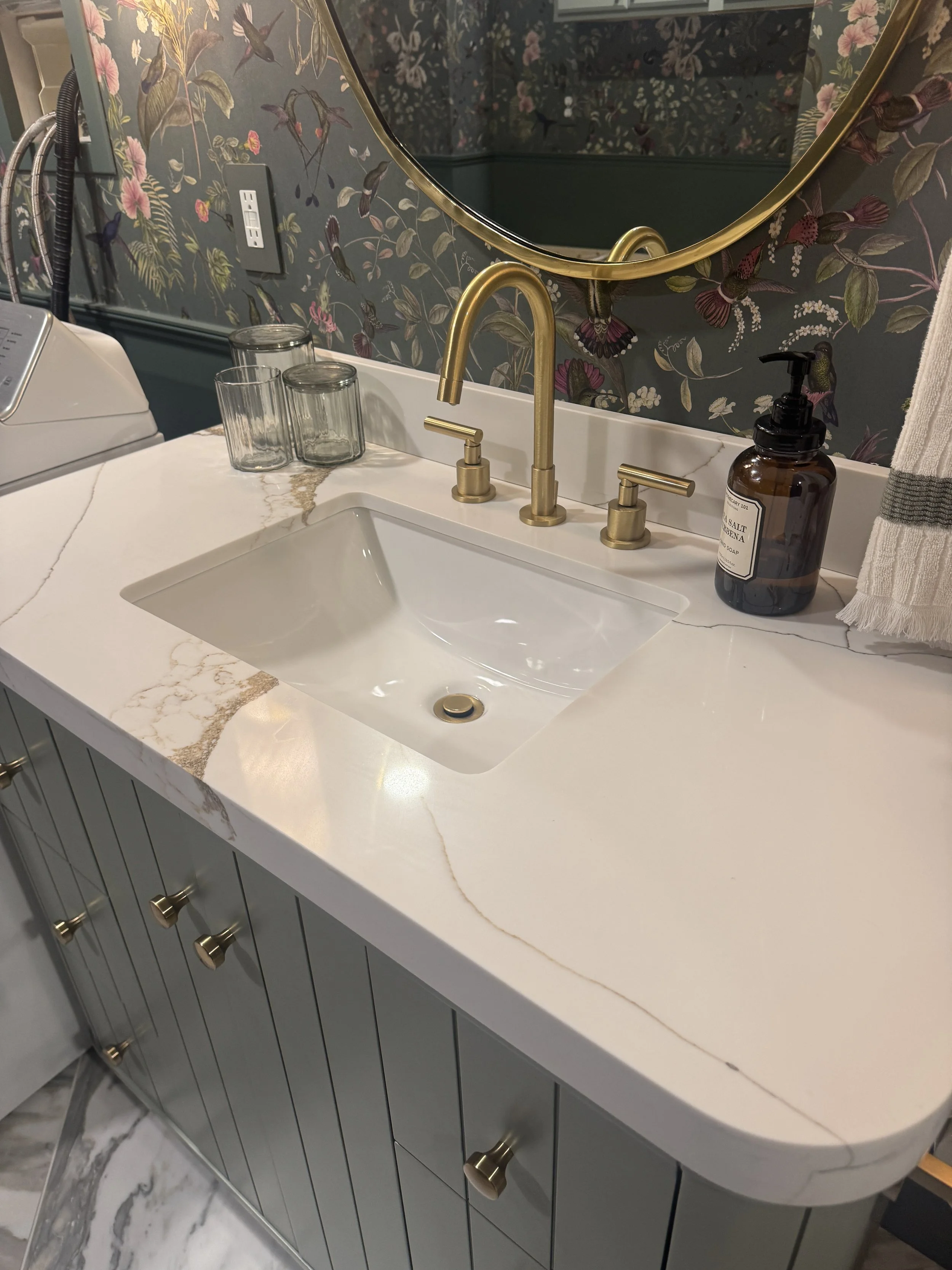 Brass widespread faucet and marble countertop detail in a Beavercreek, Ohio basement bathroom renovation with botanical wallpaper by White Oak Interiors