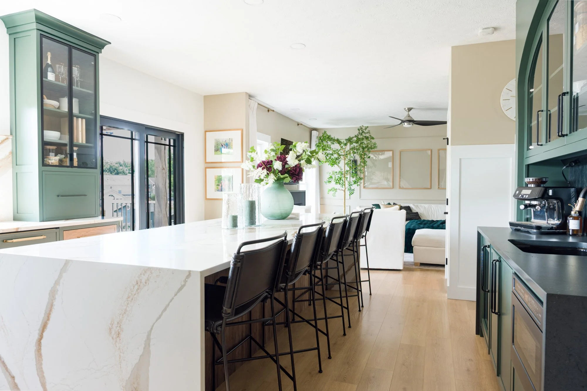 Open-concept kitchen and living space with a large waterfall quartz island, black counter stools, and white oak floors, from a luxury whole-home renovation in Beavercreek, Ohio by White Oak Interiors.