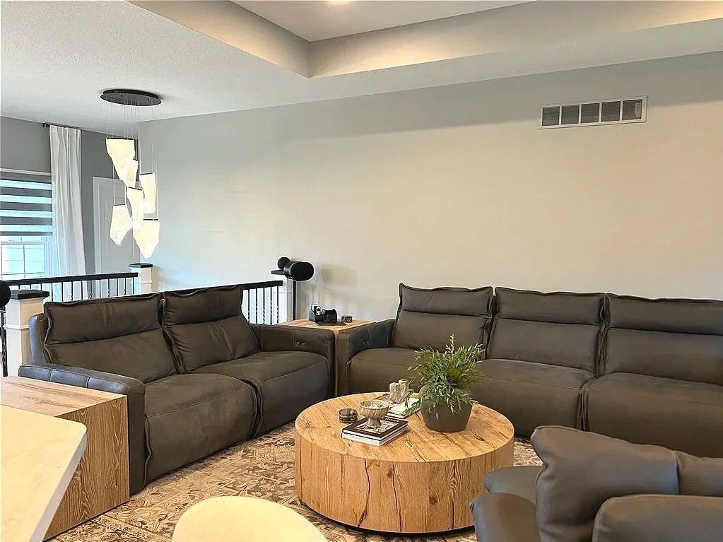 Open living room with a large sectional, round wood coffee table, tray ceiling, and an open stairway railing in a Xenia, Ohio home