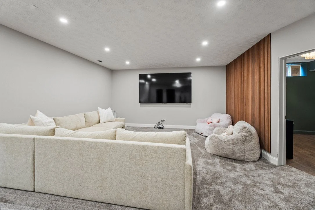 Finished basement living area with a cream sectional, wood accent wall, and wall-mounted TV in a Brookville, Ohio basement renovation.