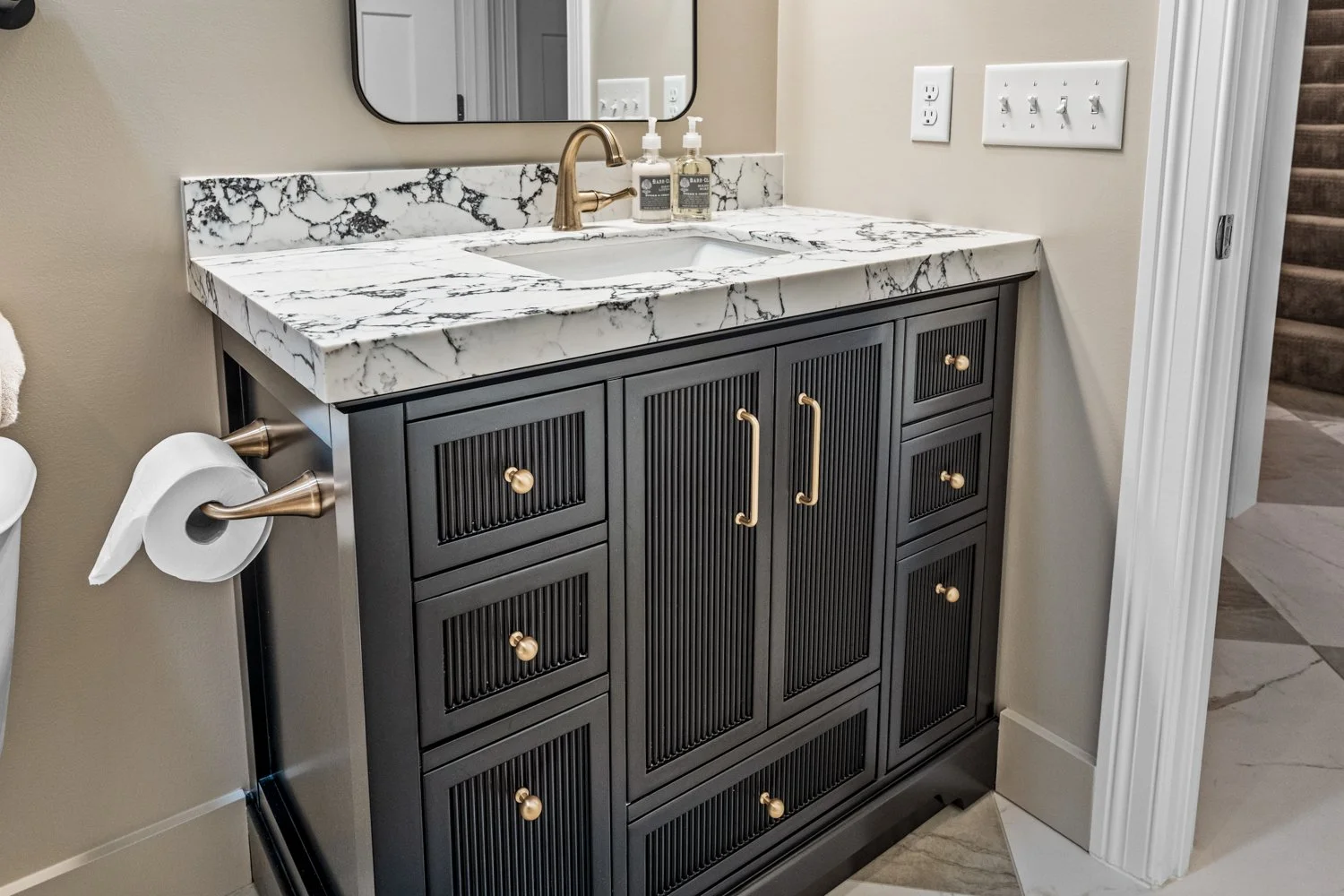 Dark fluted vanity cabinetry with brass pulls and a marble countertop, framed by soft two-tone walls in a Centerville, Ohio basement bathroom.