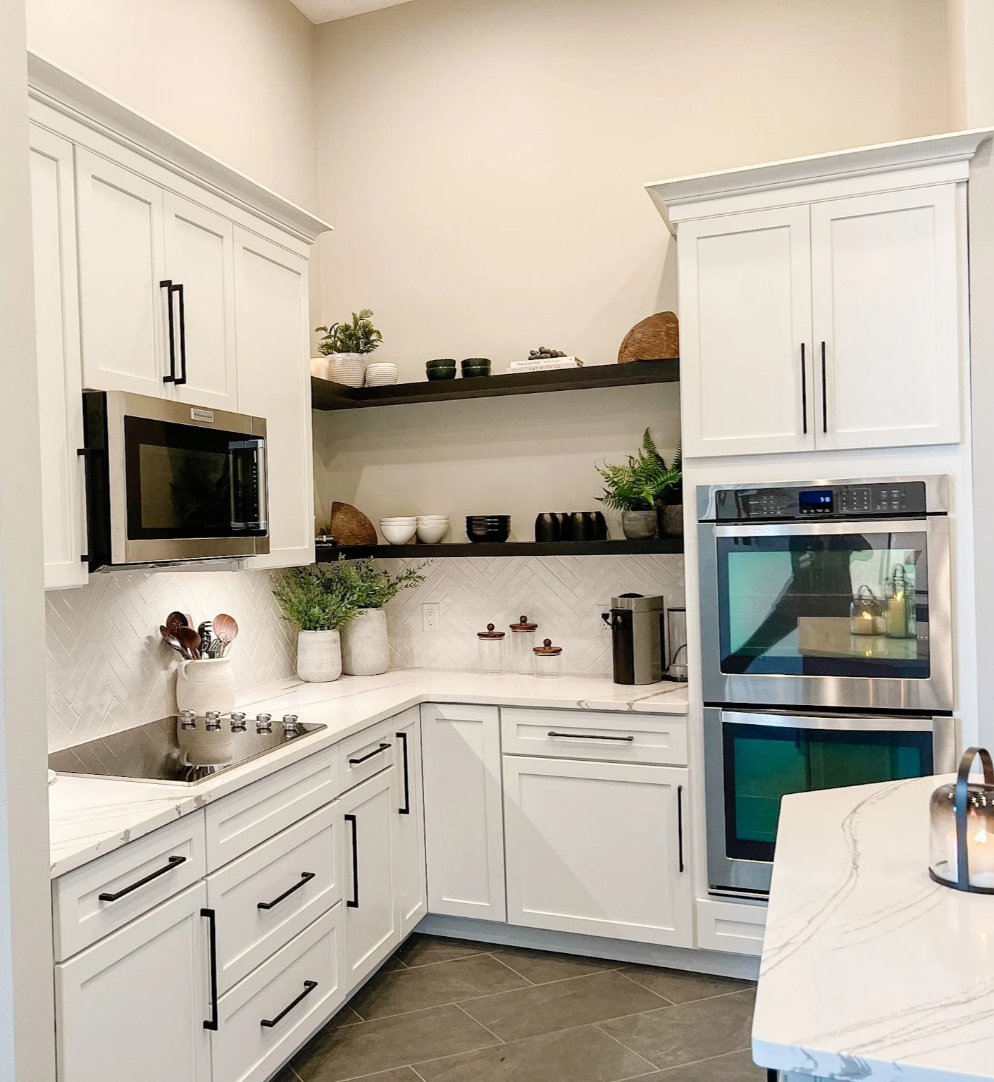 Kitchen corner with stainless double wall ovens, a cooktop, white cabinetry, a floating wood shelf, and marble-look countertops in a Centerville, Ohio home