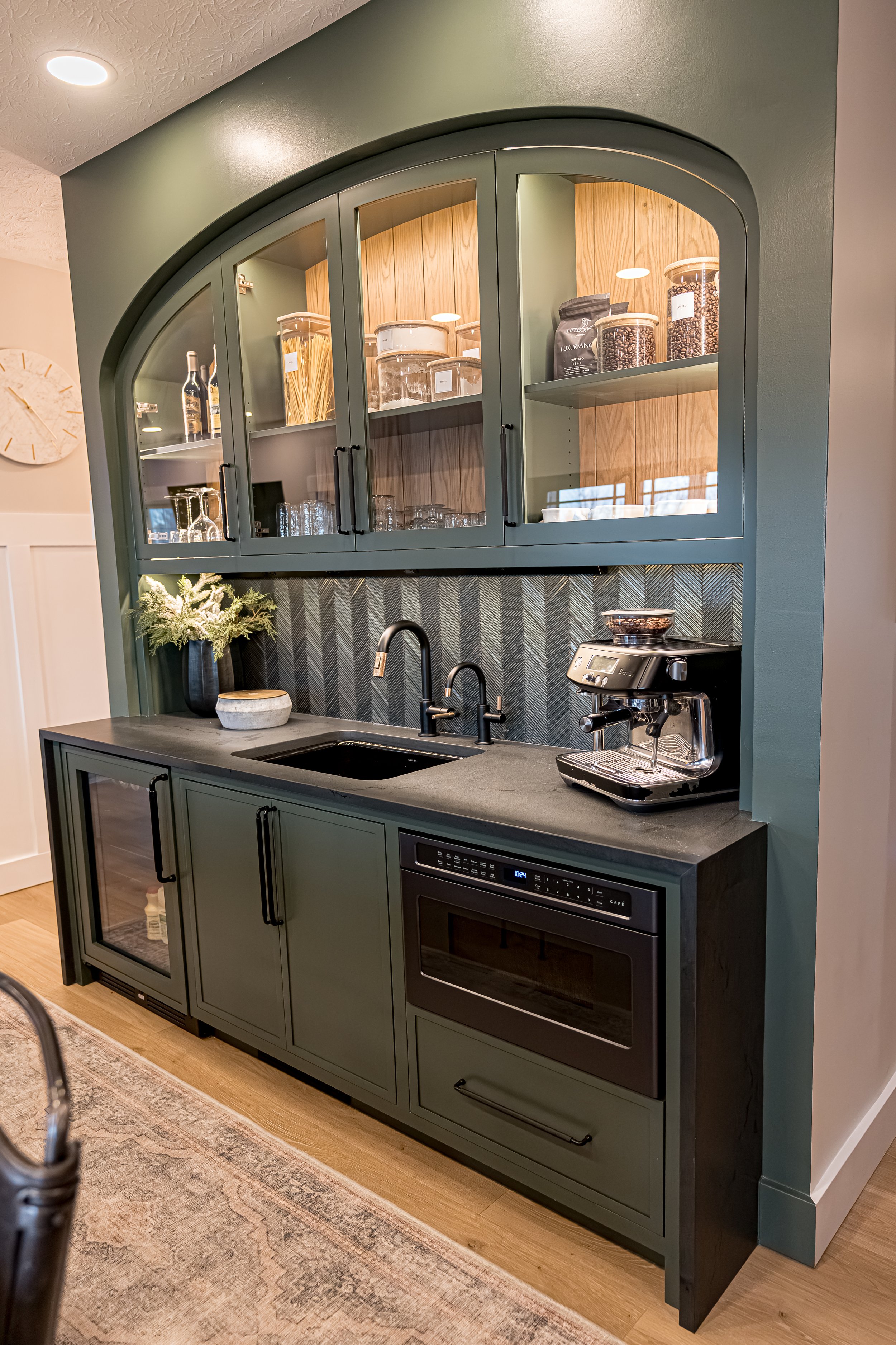 Green arched coffee bar with glass-front cabinets, espresso station, and dark stone countertop