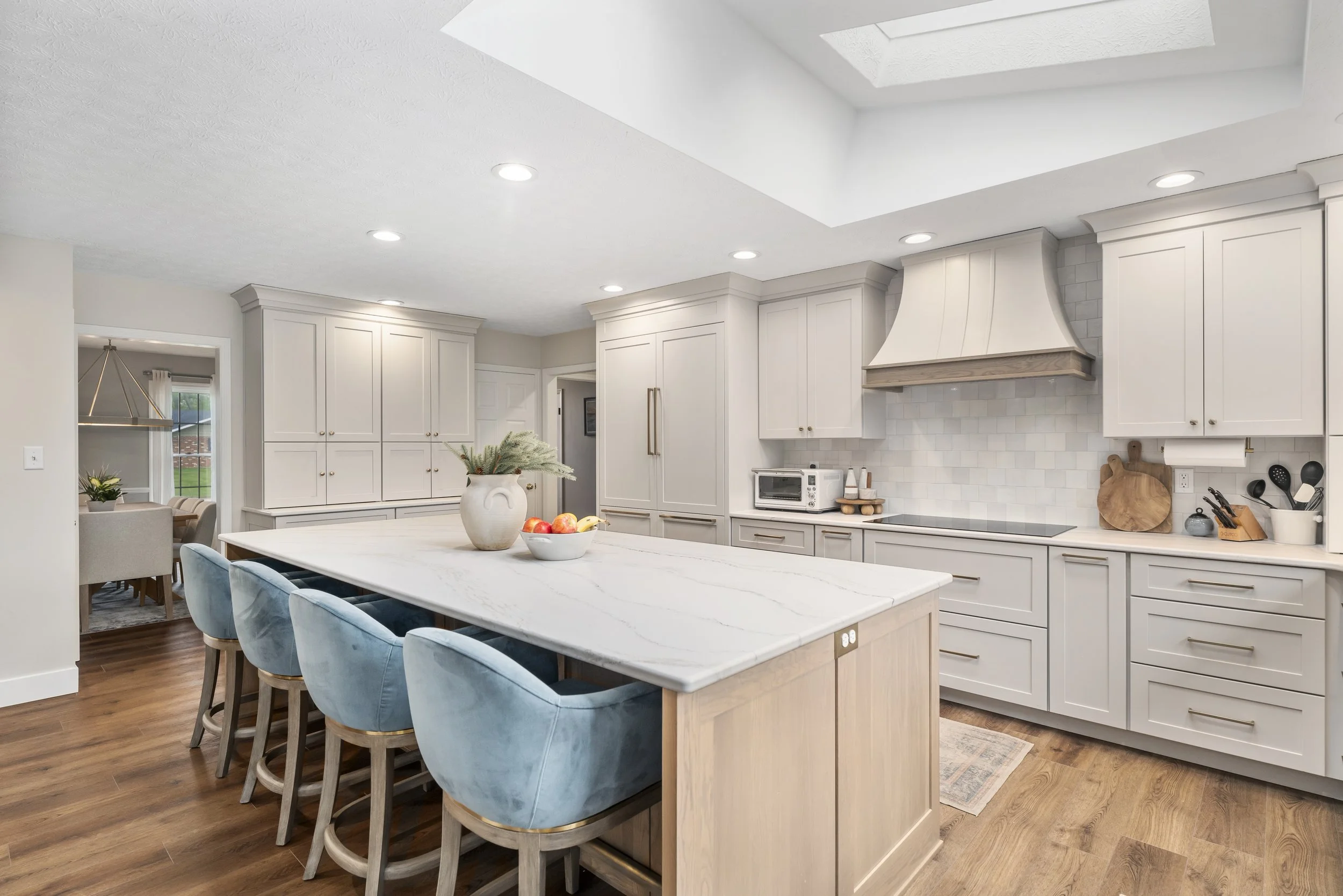 Bright white kitchen with custom wood hood, light oak island, blue velvet seating, skylights, and quartz countertops in a Piqua, Ohio renovation