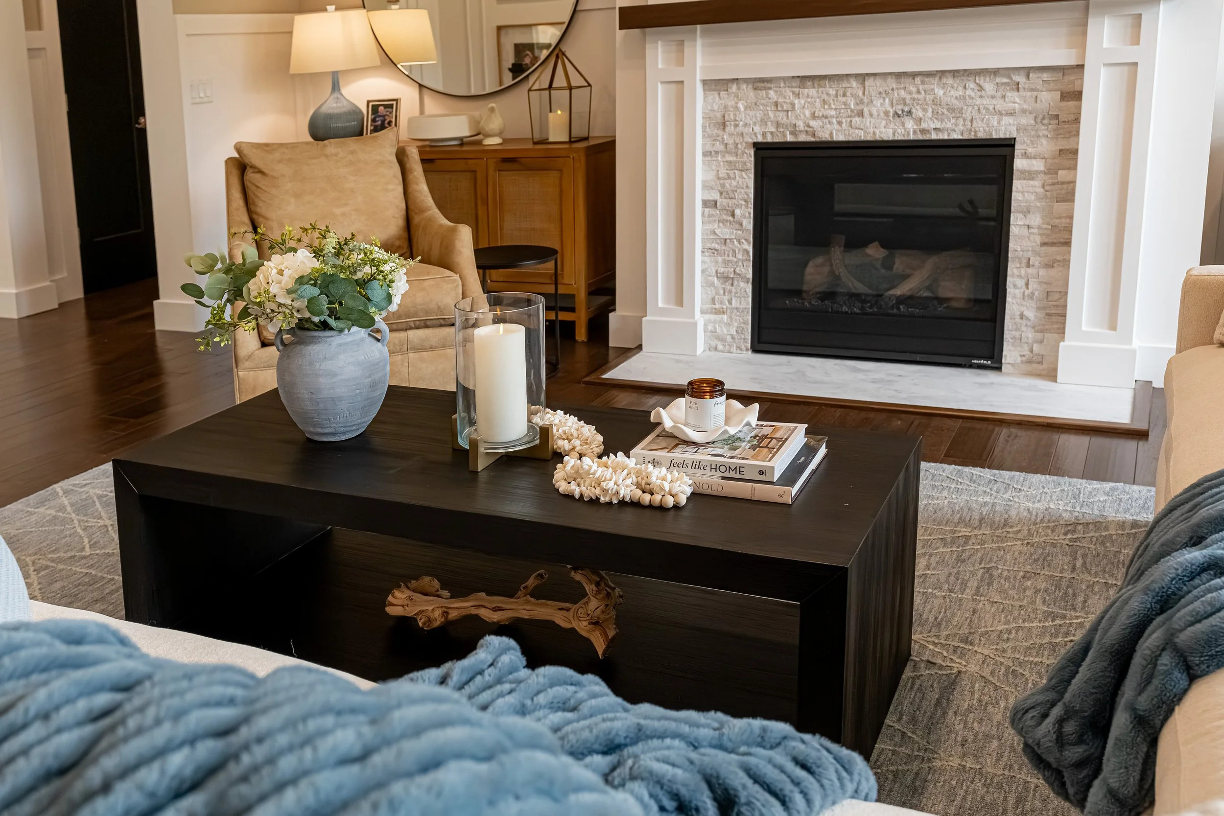 Living room seating area with a stacked stone fireplace, upholstered armchair, and styled wood coffee table in a Centerville home renovation.