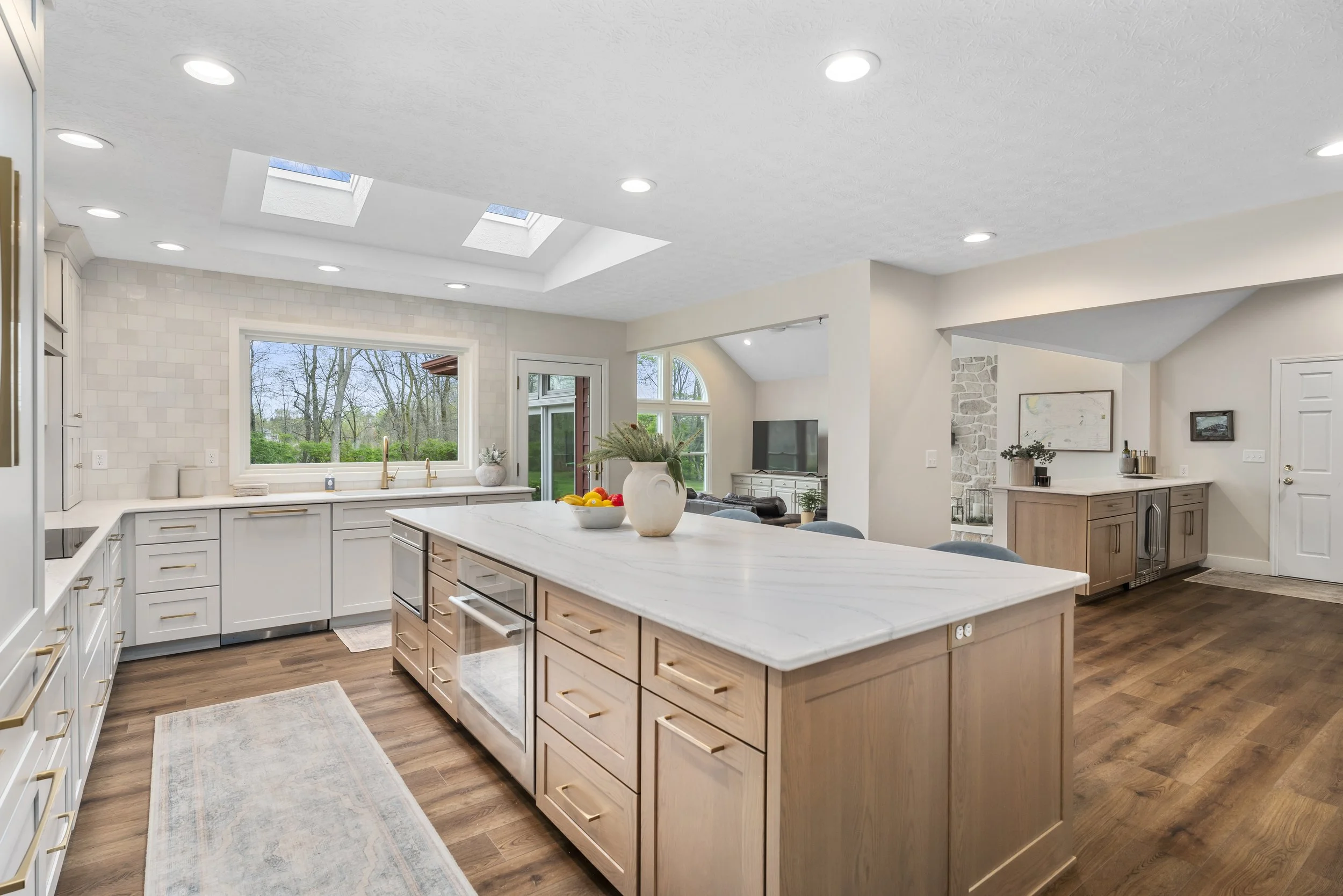 Open-concept kitchen with light wood island, white quartz countertop, skylights, and sightlines into the dining and living areas