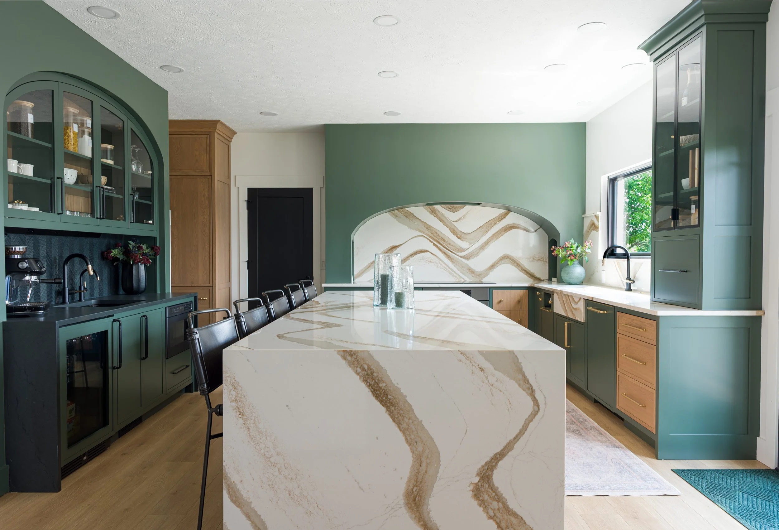 Modern luxury kitchen in a Beavercreek whole-home renovation featuring a waterfall-edge quartz island, sage green cabinetry, and an arched marble backsplash by White Oak Interiors.