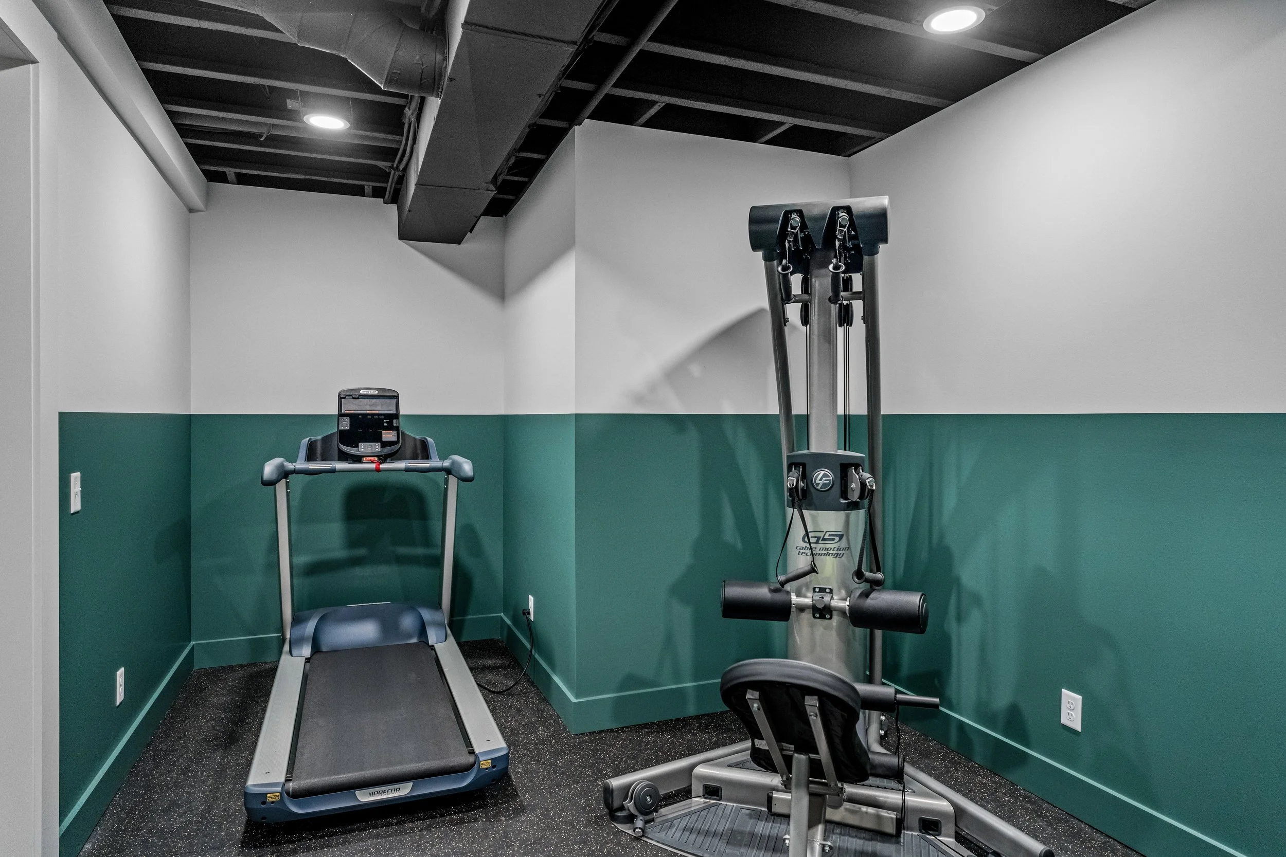Finished basement home gym in Centerville, Ohio with treadmill, weight machine, green accent walls, and black-painted ceiling by White Oak Interiors