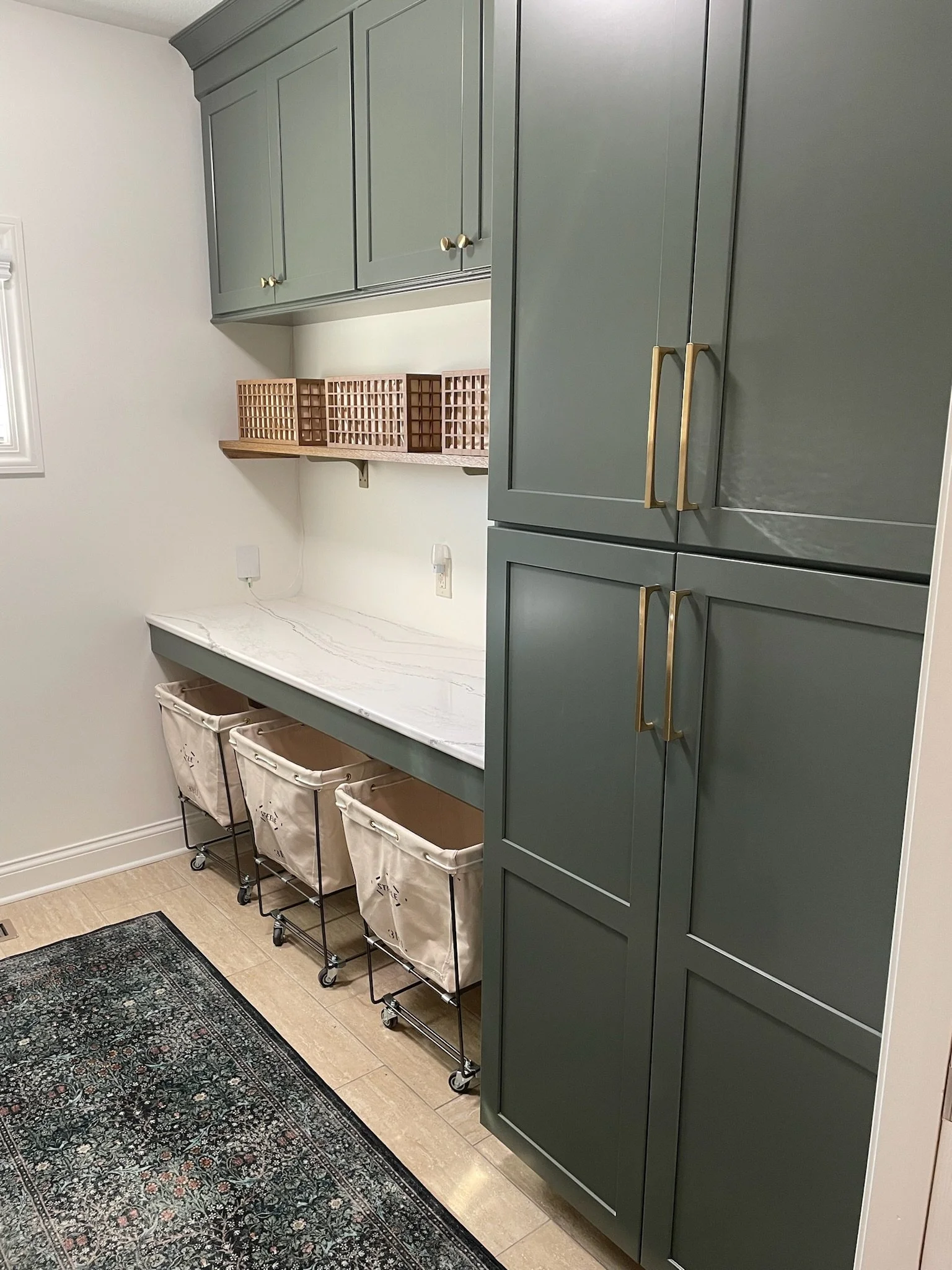 Custom green laundry cabinetry with a quartz folding counter, wood shelf, and built-in pull-out hamper storage in a Beavercreek, Ohio laundry room