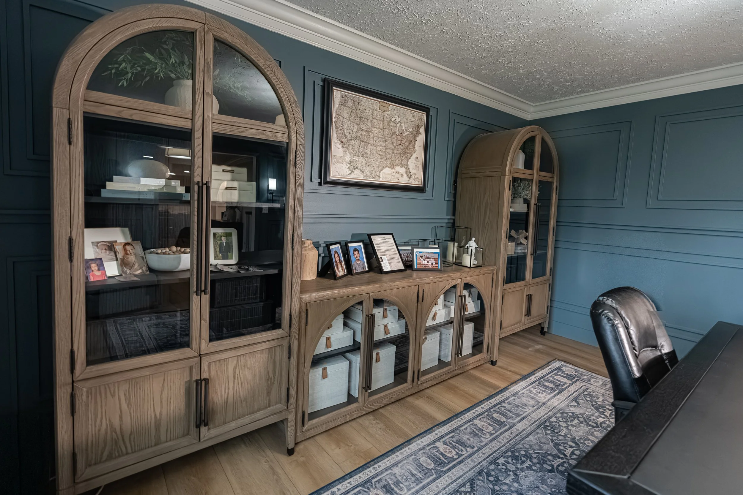 Home office with deep blue paneled walls and an arched wood display cabinet, designed by White Oak Interiors in the Dayton, Ohio area.