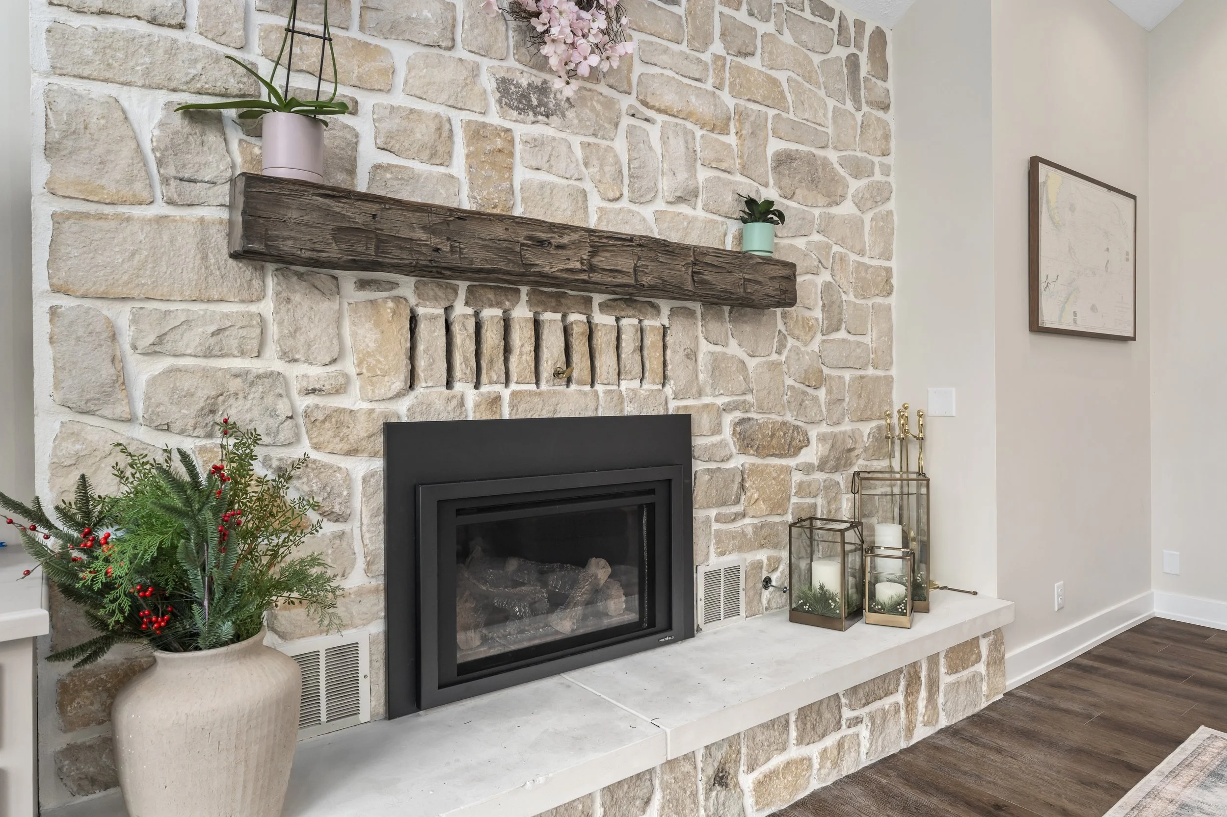 Refreshed stone fireplace with a rustic wood beam mantle, new black insert, and brightened stonework as the living room focal point