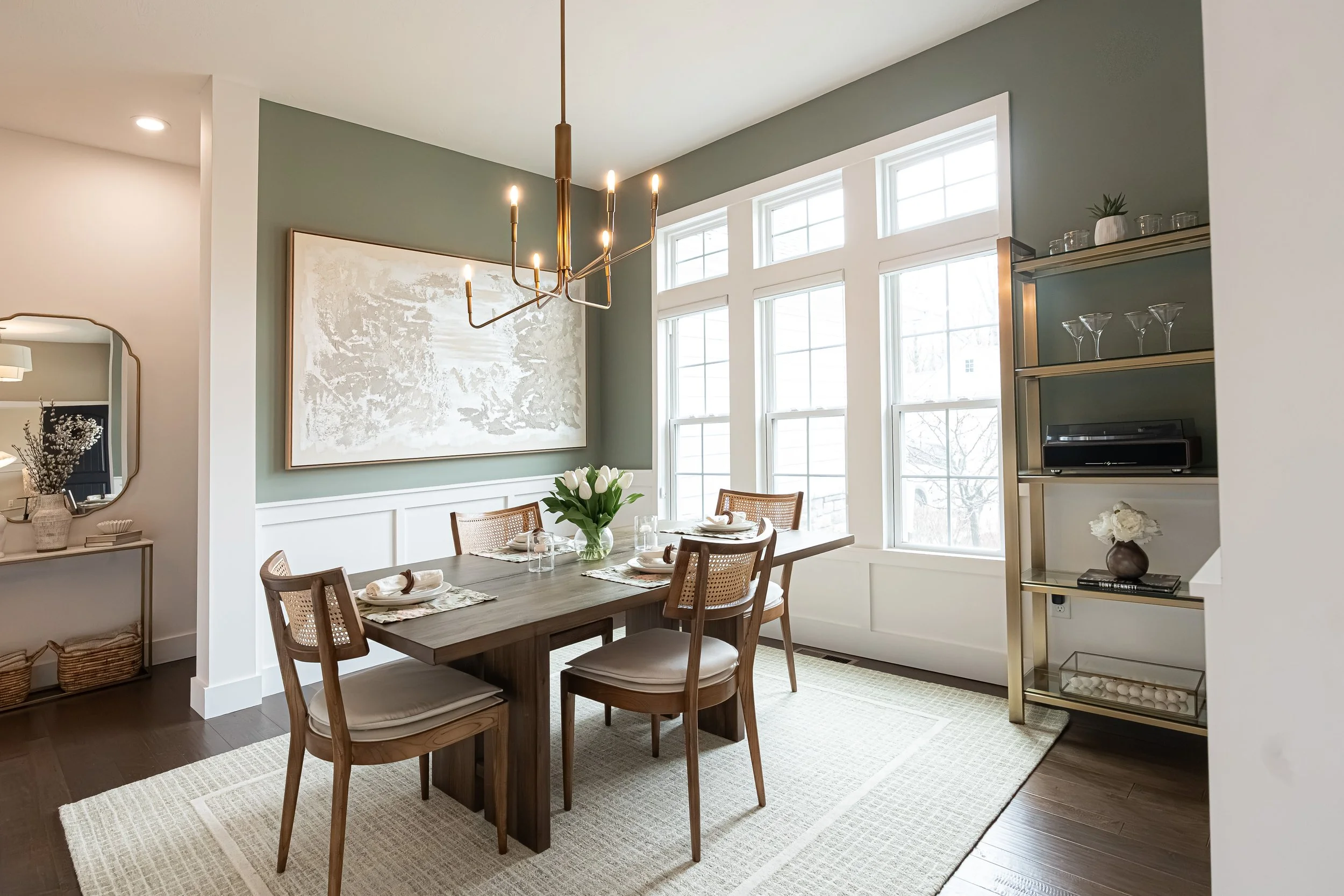 Formal dining room with a wood table, cane-back chairs, a brass linear chandelier, and sage green walls in a Centerville home renovation.
