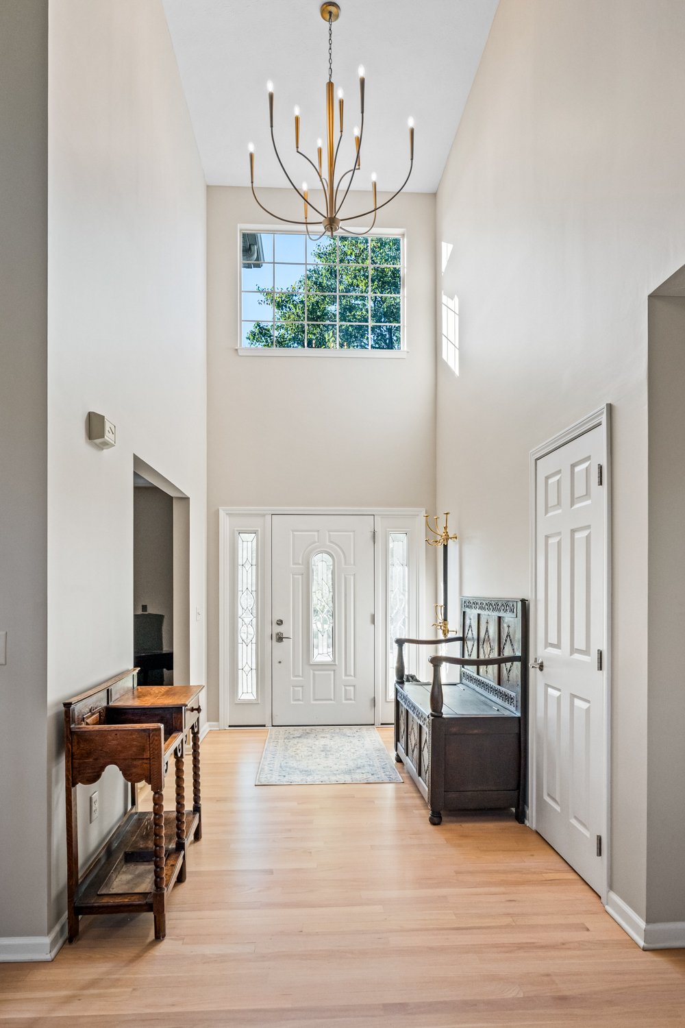 Entry foyer with a white front door, soaring ceiling, brass chandelier, and a wood console table in a Beavercreek, Ohio remodel.