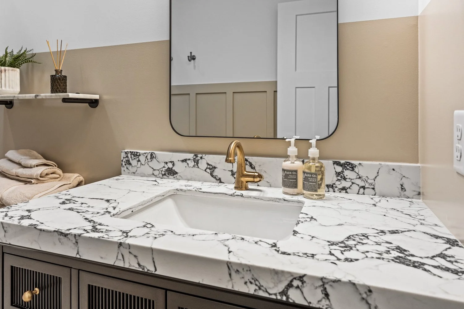 White-and-black marble countertop with an undermount sink and gooseneck brass faucet against a dark reeded vanity in a Centerville, Ohio basement bathroom.