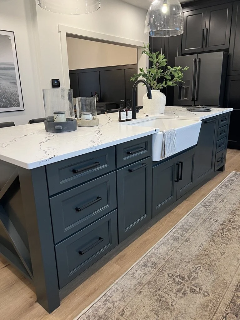 Dark green kitchen cabinetry with a white farmhouse apron-front sink, quartz countertop, and black faucet and hardware in a Springboro, Ohio home