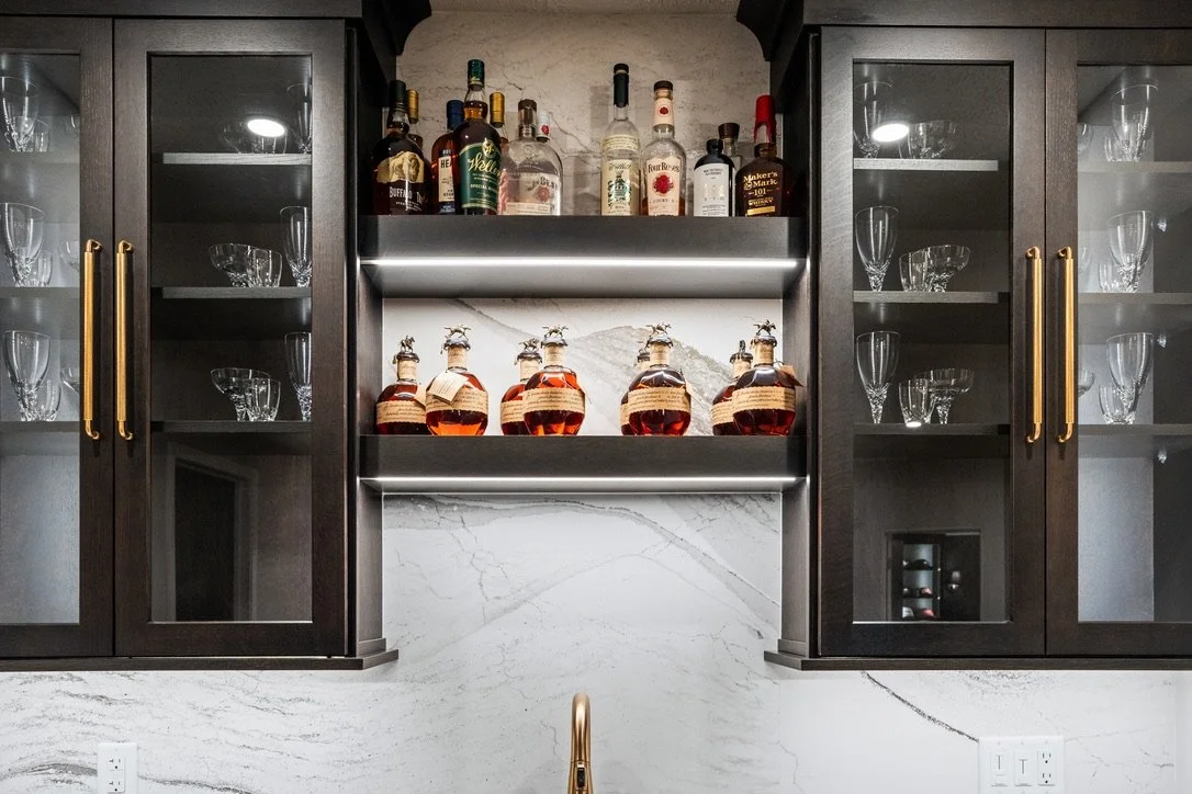 Basement bar with backlit glass-front cabinets, open display shelving, and a marble backsplash in a Brookville, Ohio basement renovation.
