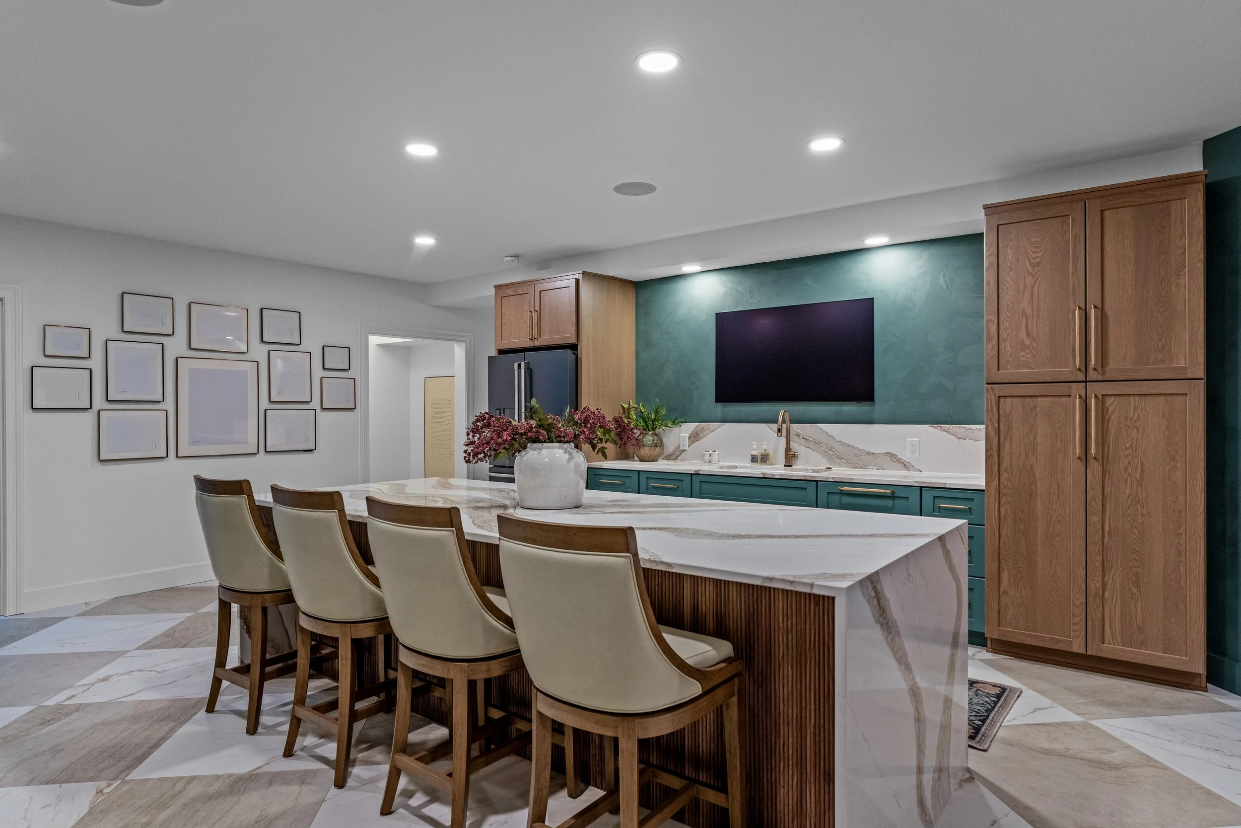 Finished basement kitchen in the Dayton, Ohio area with a white oak waterfall-edge island, teal cabinetry, and a gallery wall by White Oak Interiors