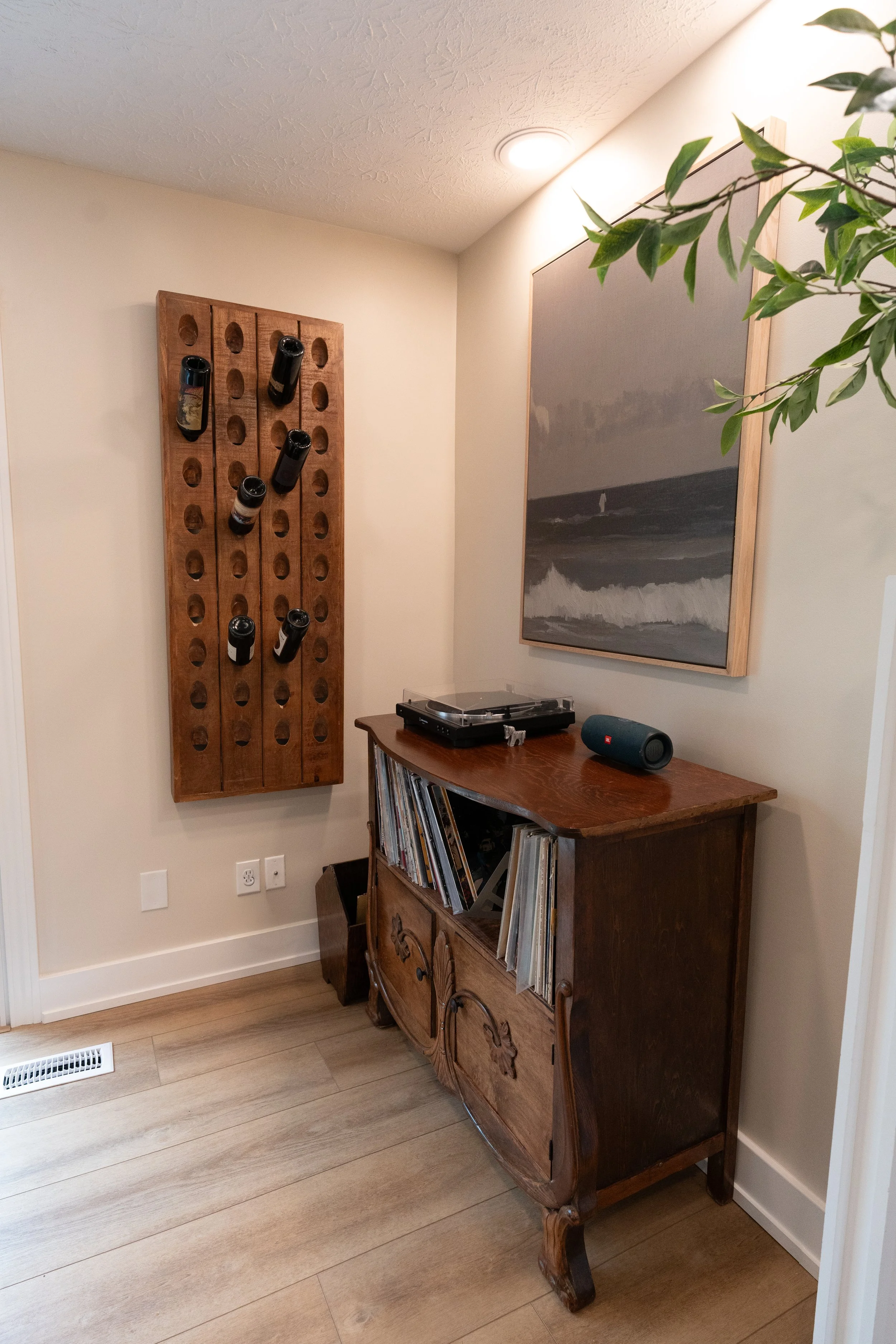 Styled corner with a wall-mounted wine rack, antique record cabinet, and framed art in a Centerville home remodel.