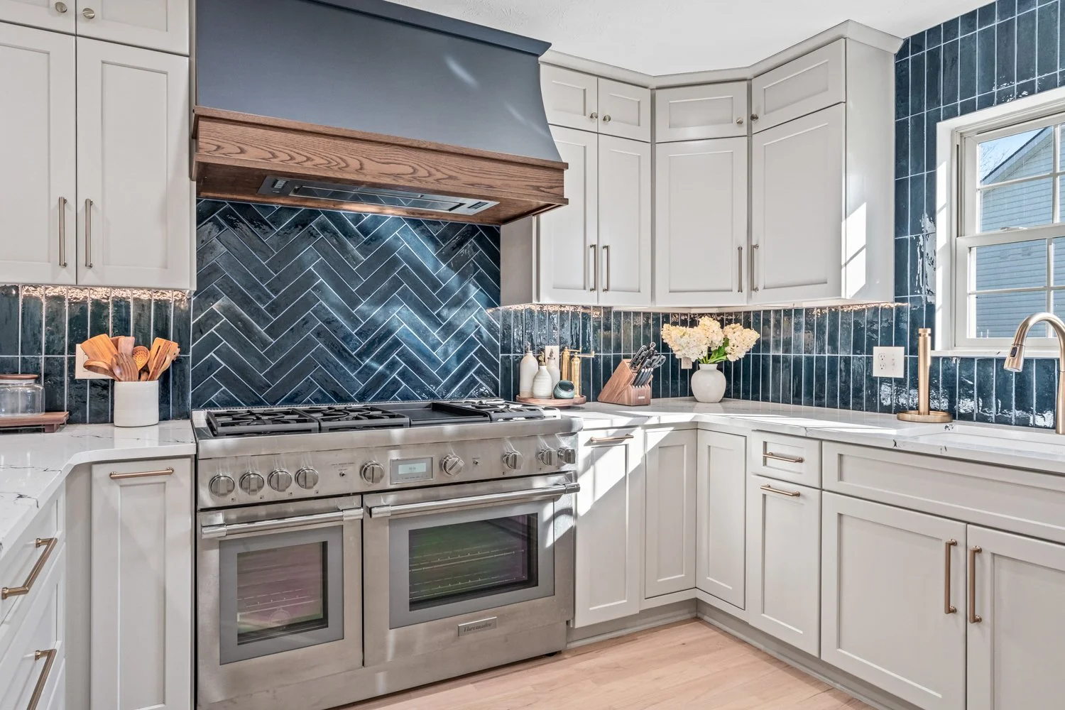 Stainless gas range beneath a custom navy wood-trimmed hood with blue herringbone tile in a Beavercreek, Ohio kitchen remodel.