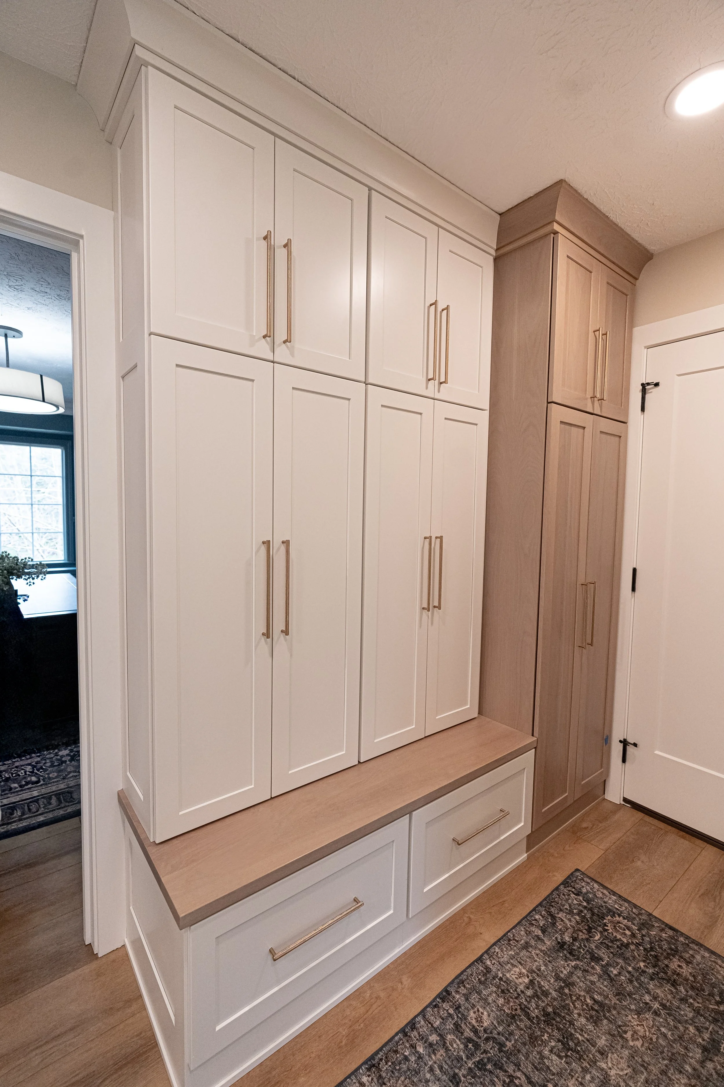 Mudroom with floor-to-ceiling natural wood cabinetry, brass pulls, and a built-in bench with storage in a Centerville remodel.