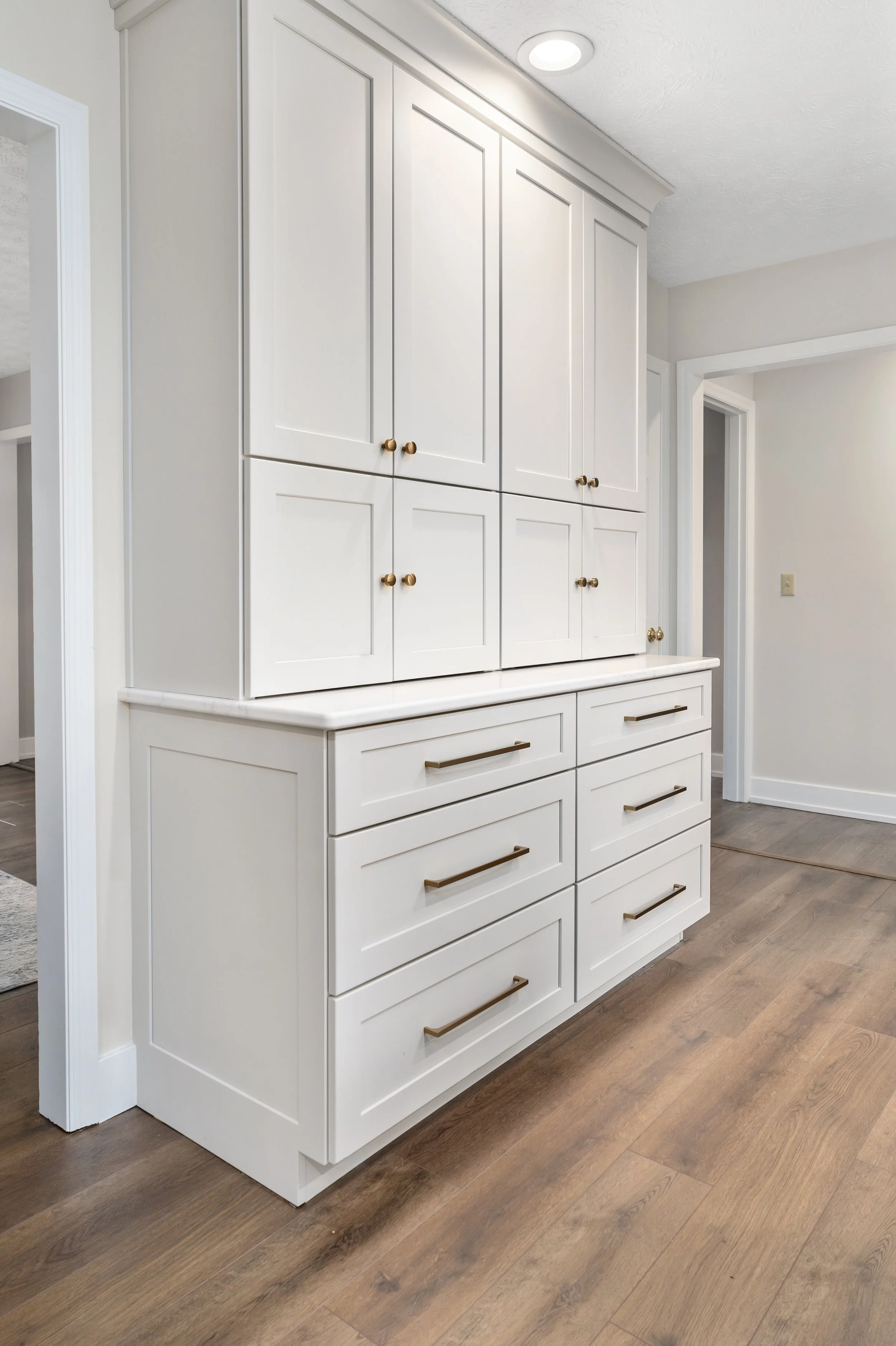 Custom floor-to-ceiling pantry cabinetry with white shaker doors, deep drawers, and brass hardware, added for extra kitchen storage