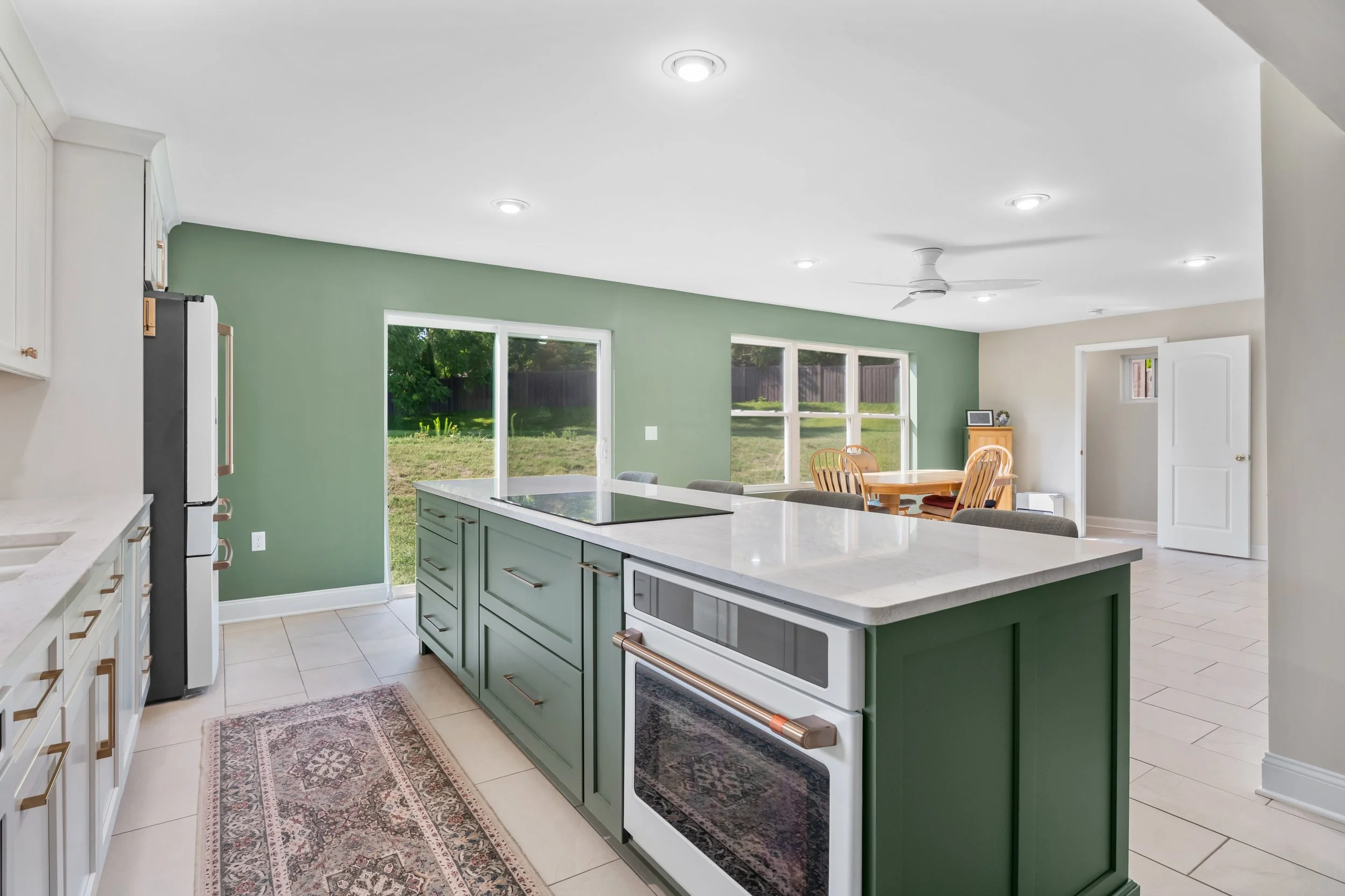 Open-concept kitchen and home addition in Springfield, Ohio with an evergreen island, cooktop facing the room, and dining area by White Oak Interiors